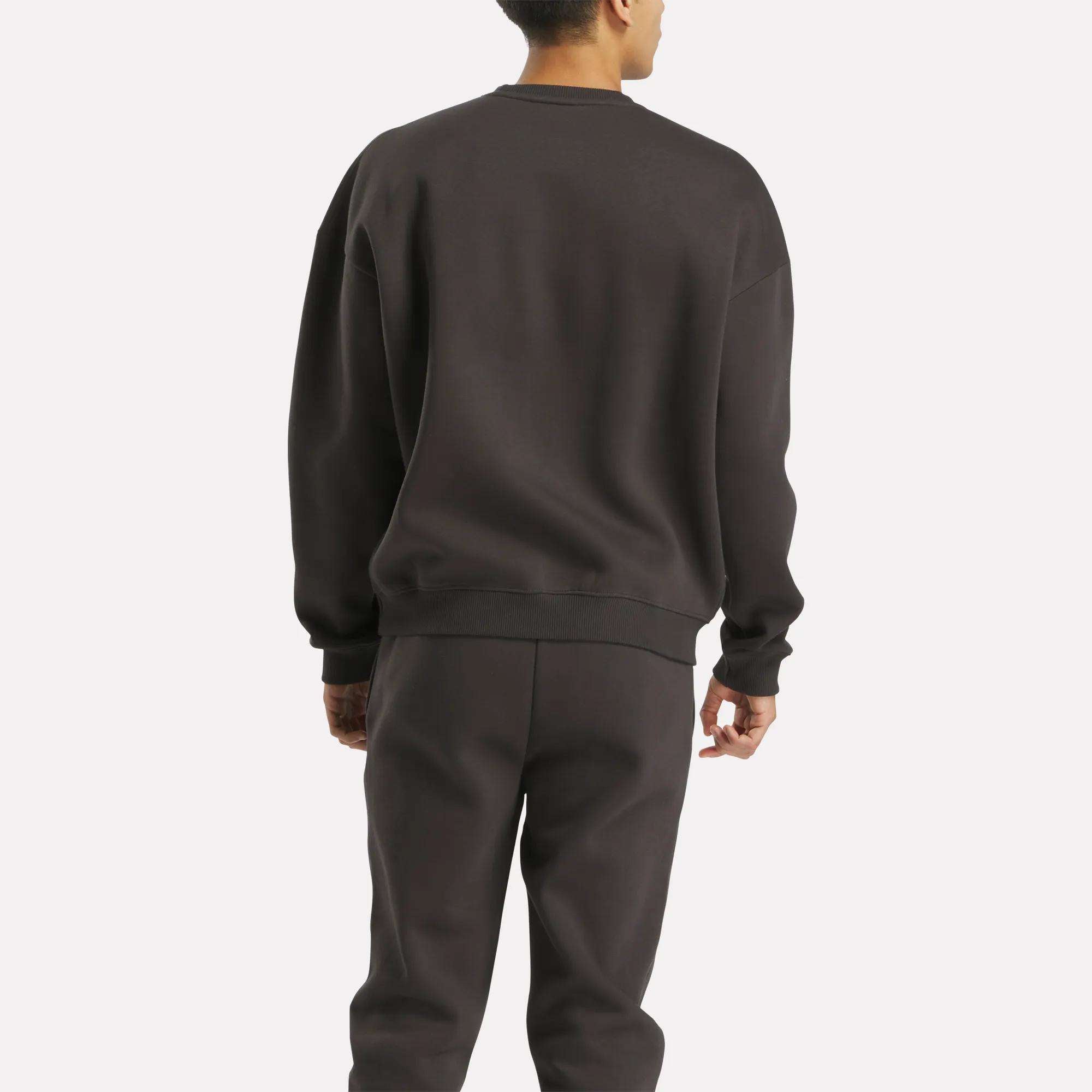 A person faces away from the camera, wearing a Reebok Men's Varsity Sweatshirt against a plain, light background.