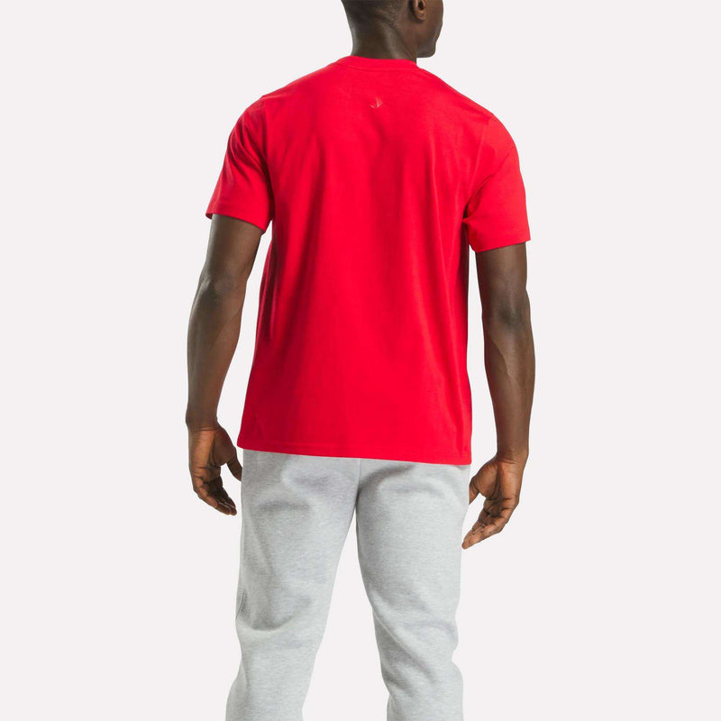 A man faces away from the camera in a Reebok Men's Big Logo Crewneck Short Sleeve Tee in bright red and light gray sweatpants, set against a plain white background.