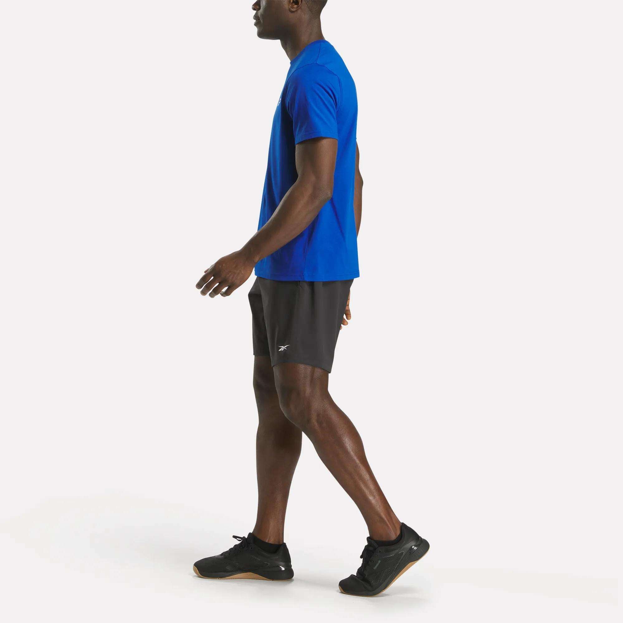 A man wearing a blue Reebok Men's Small Logo Crewneck Short Sleeve T-Shirt and shorts is walking.