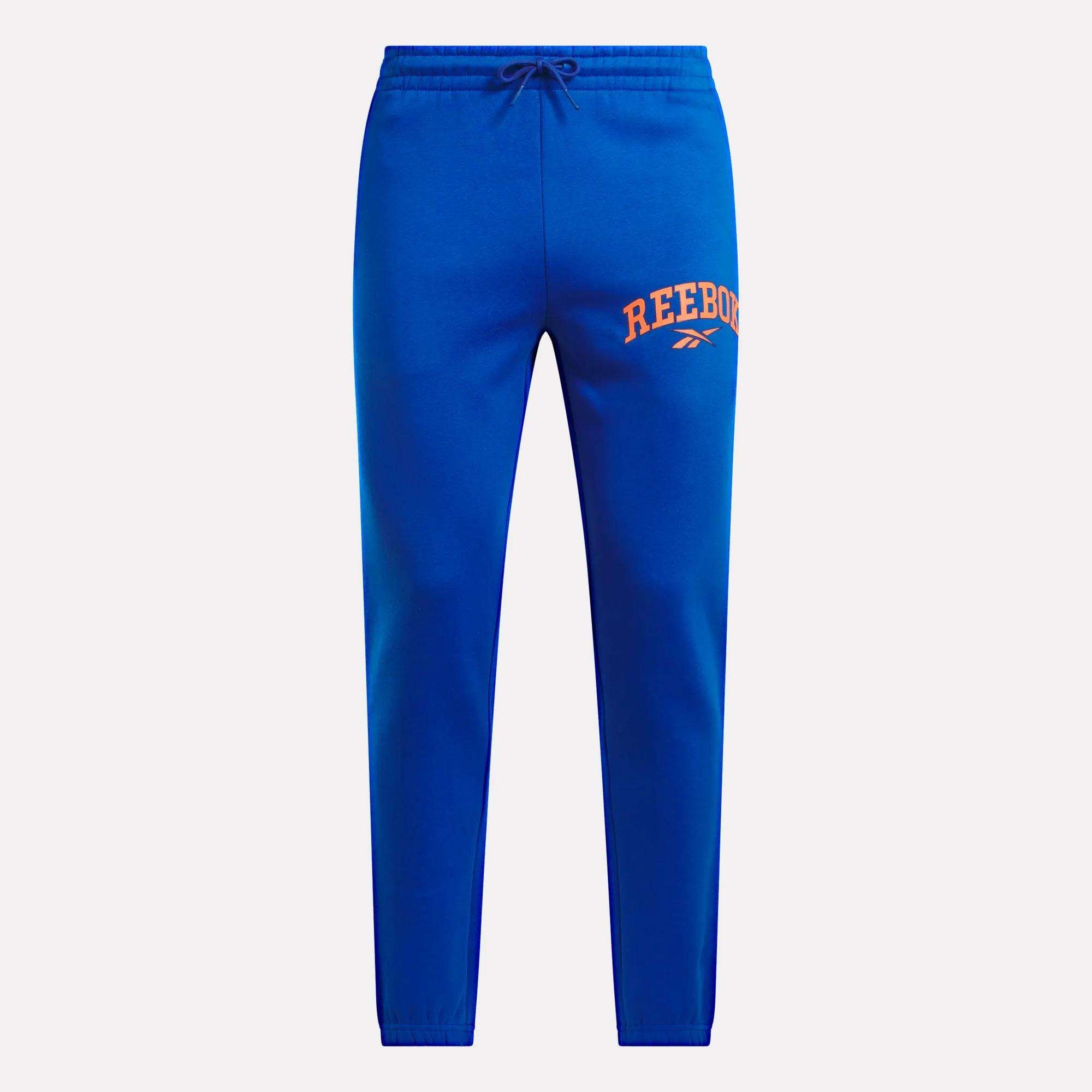 Men's Varsity Joggers by Reebok in bright blue, featuring a relaxed fit, drawstring waist, and an orange REEBOK logo with a small white symbol on the left thigh, shown against a plain white background.
