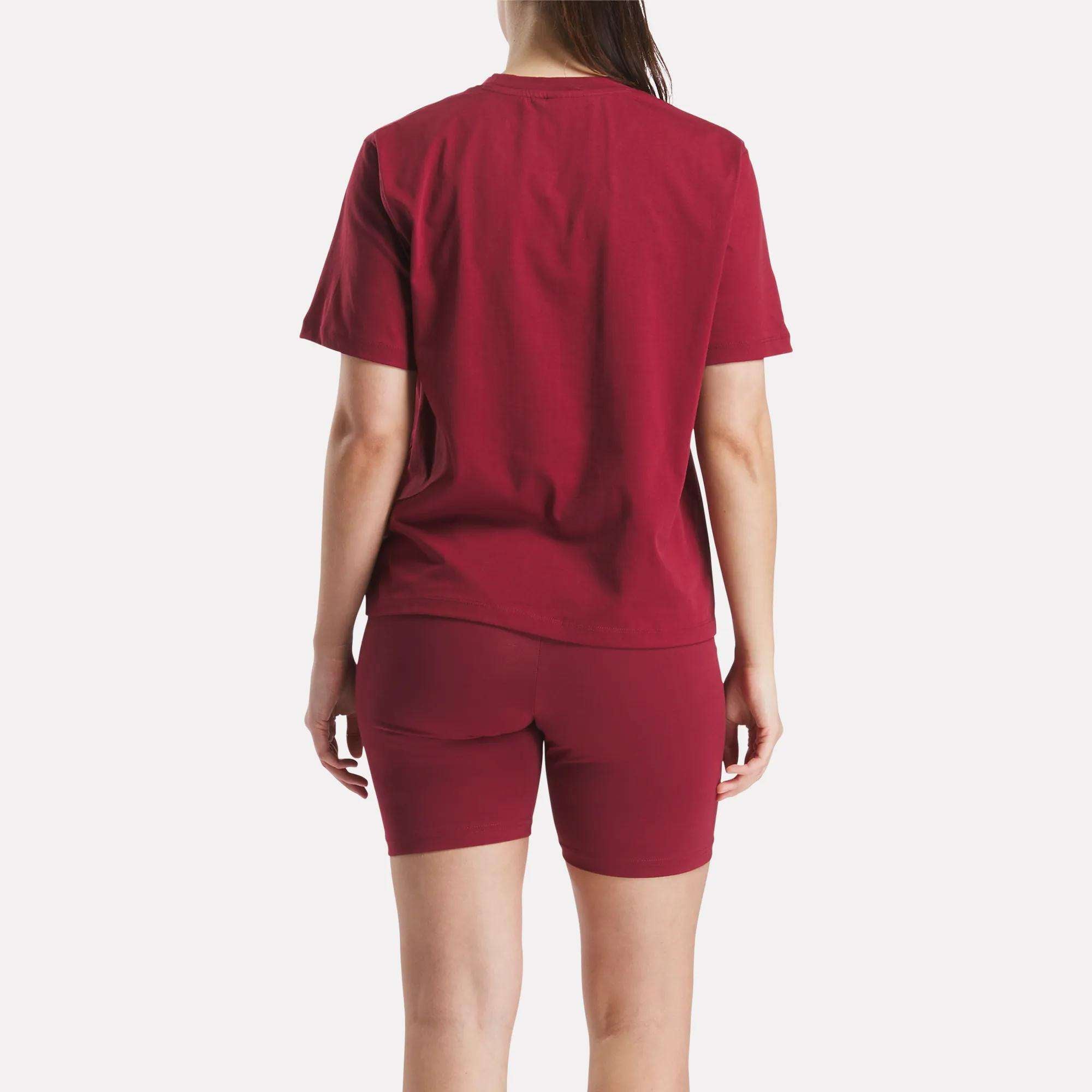 A person faces away from the camera, wearing a matching Reebok Women's Big Logo Oversized Crew Short Sleeve Tee and maroon shorts. The scene is set against a plain white background.
