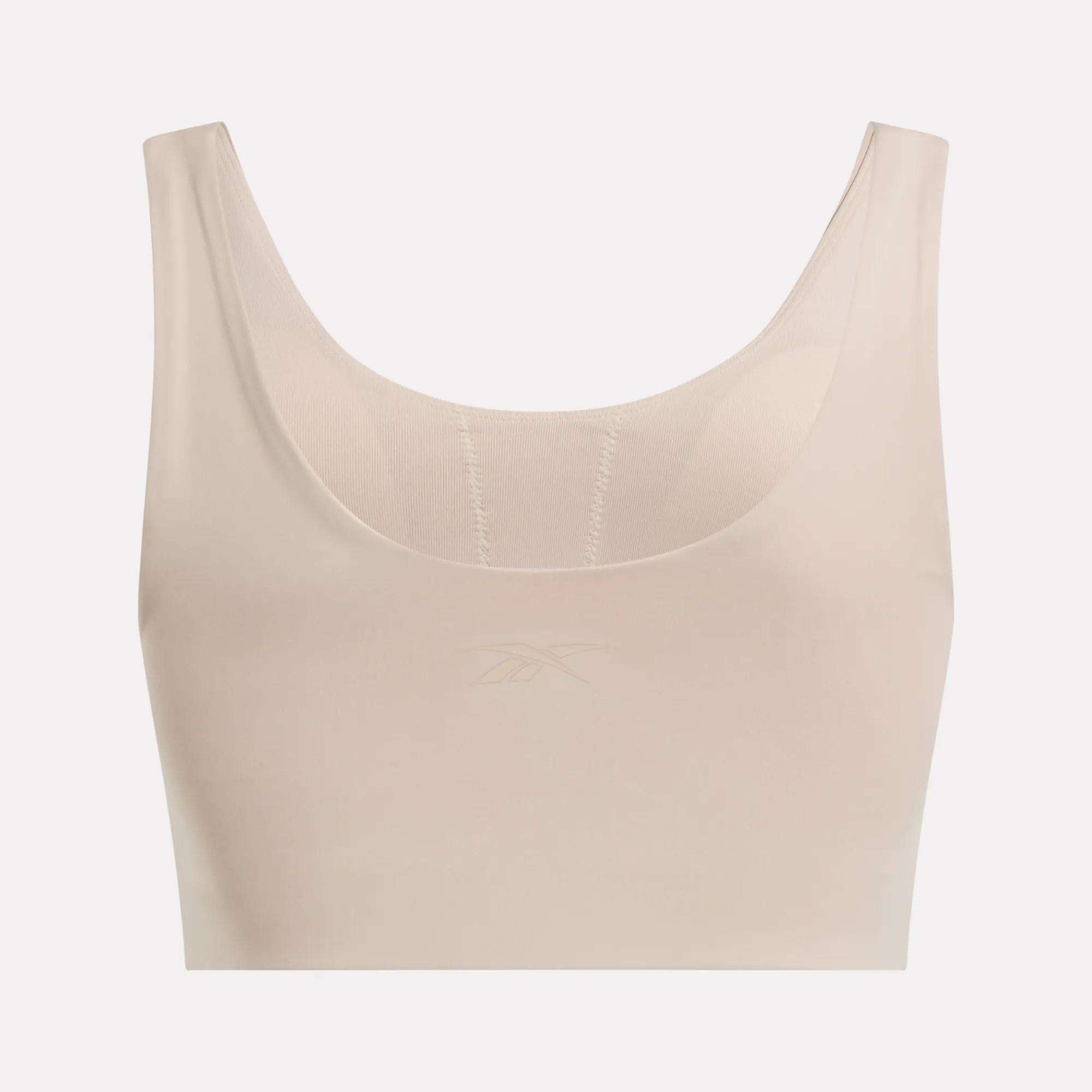The Reebok Women's Yoga V-Neck Bra in beige features a sleeveless, seamless design with medium-impact support, a scoop neckline, and a subtle front logo. Ideal for studio workouts. Set against a plain white background.