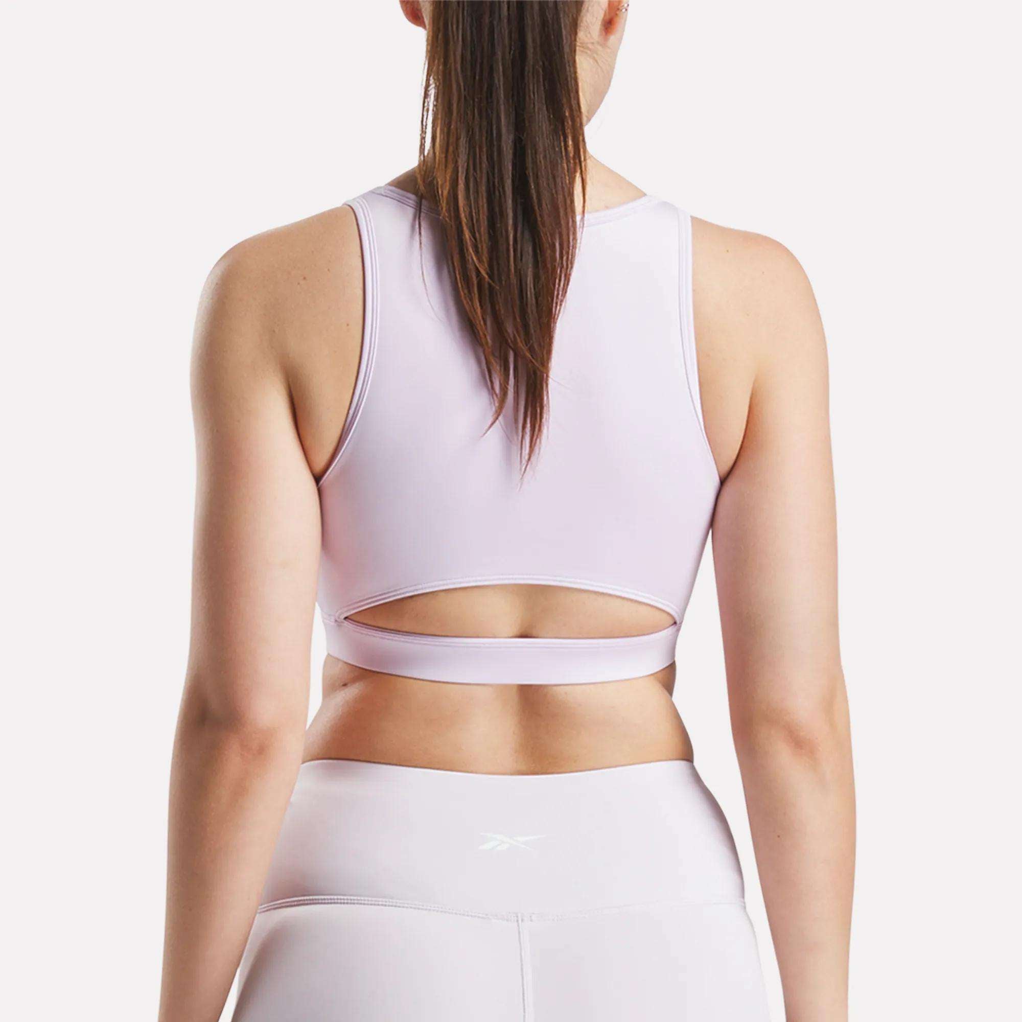 A woman is shown from the back wearing Reebok's Women's Core High-Impact Bra in light pink, featuring sweat-wicking fabric and a stylish cut-out above the waistband. Perfect for high-impact training, it pairs with matching leggings.