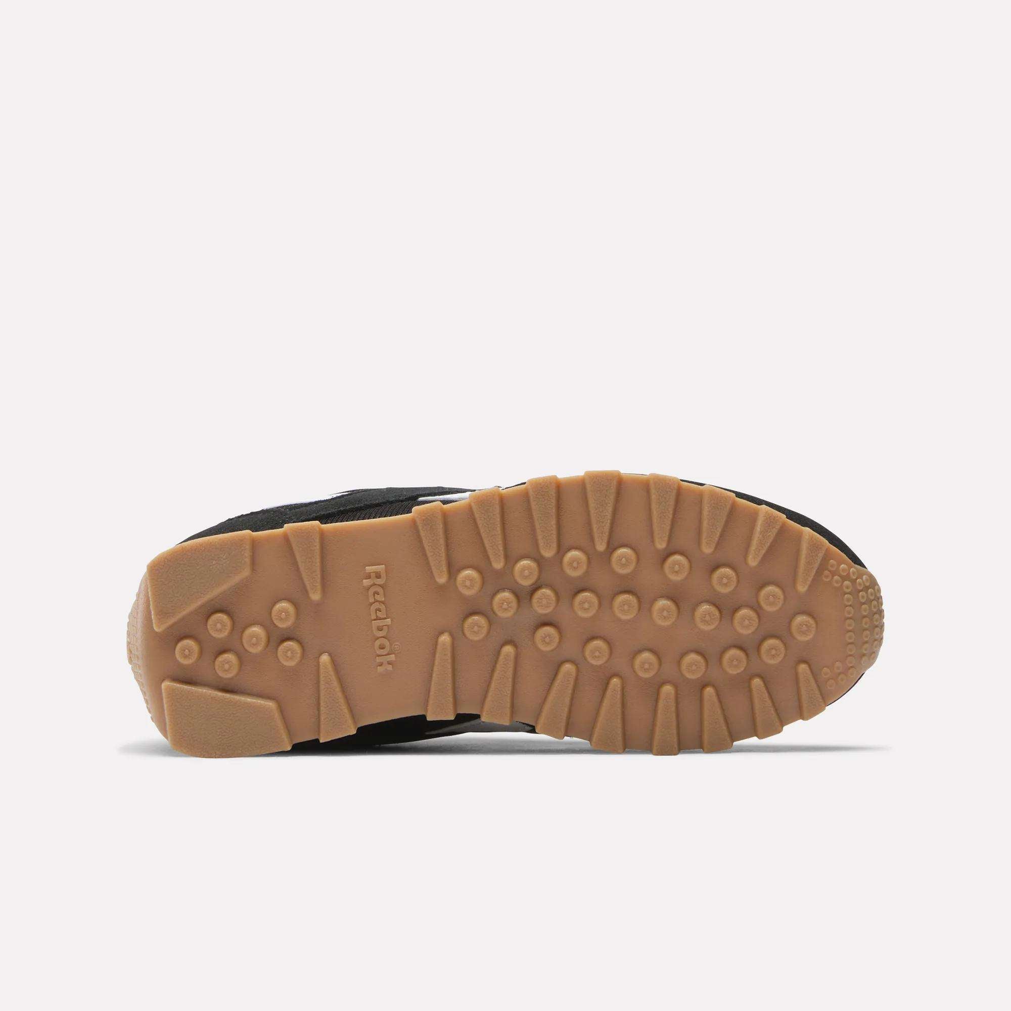 The image shows the bottom view of Reebok Classic AZ Shoes for little kids, with a tan rubber sole featuring textured grips and the Reebok logo. The partially visible black upper and foam cushioning provide comfort for young feet.