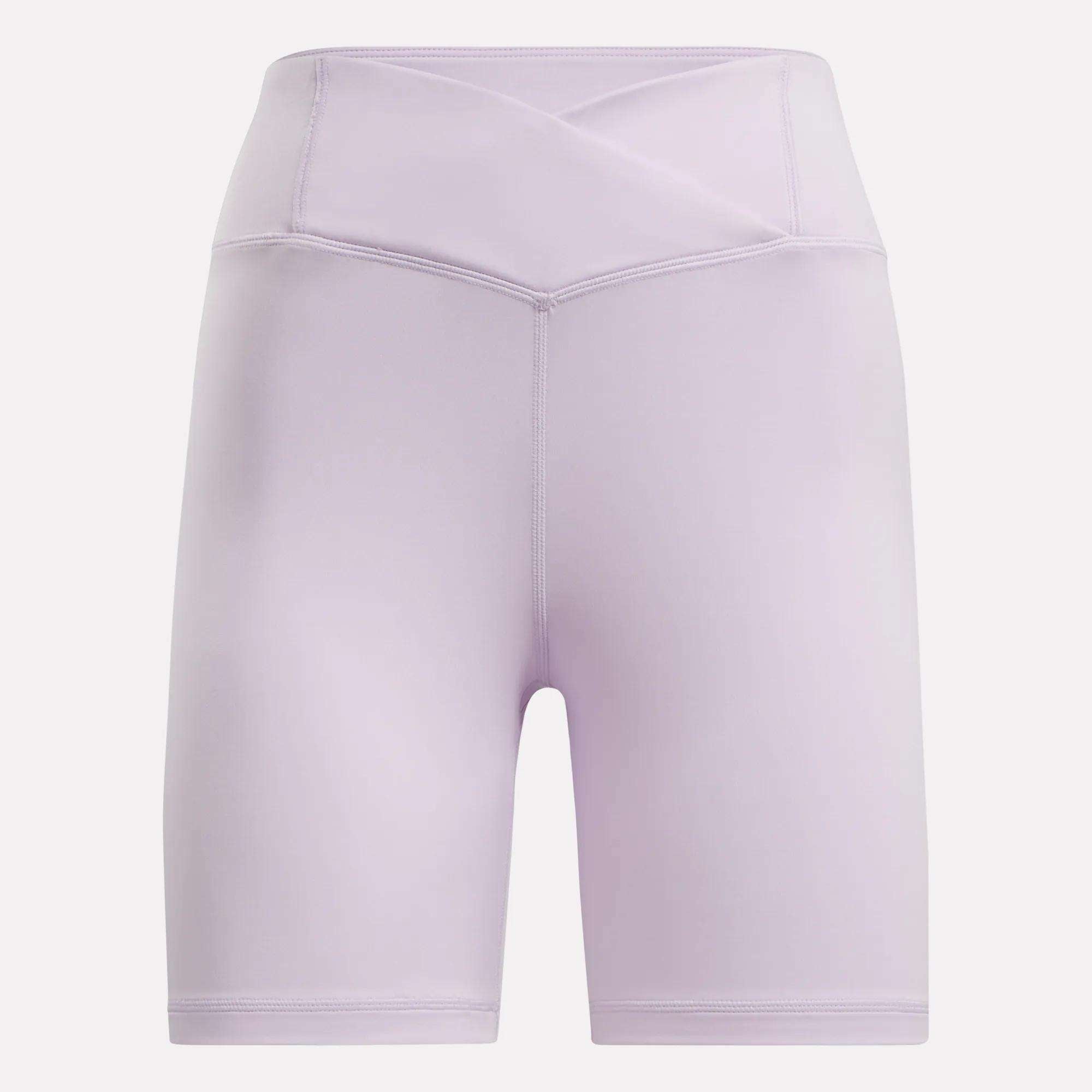 Women's Core High-Rise Cycle Shorts by Reebok in light purple, featuring a crossover waistband and visible stitching, made from sweat-wicking fabric. Shown against a plain white background.
