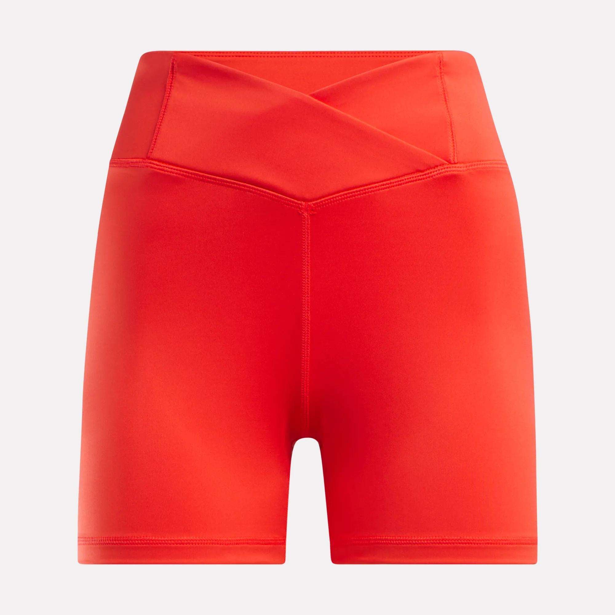 The Reebok Women's Core High-Rise Shorts feature a crossover waistband and smooth, sweat-wicking fabric. Perfect for workouts, these bright red shorts are shown against a plain white background.