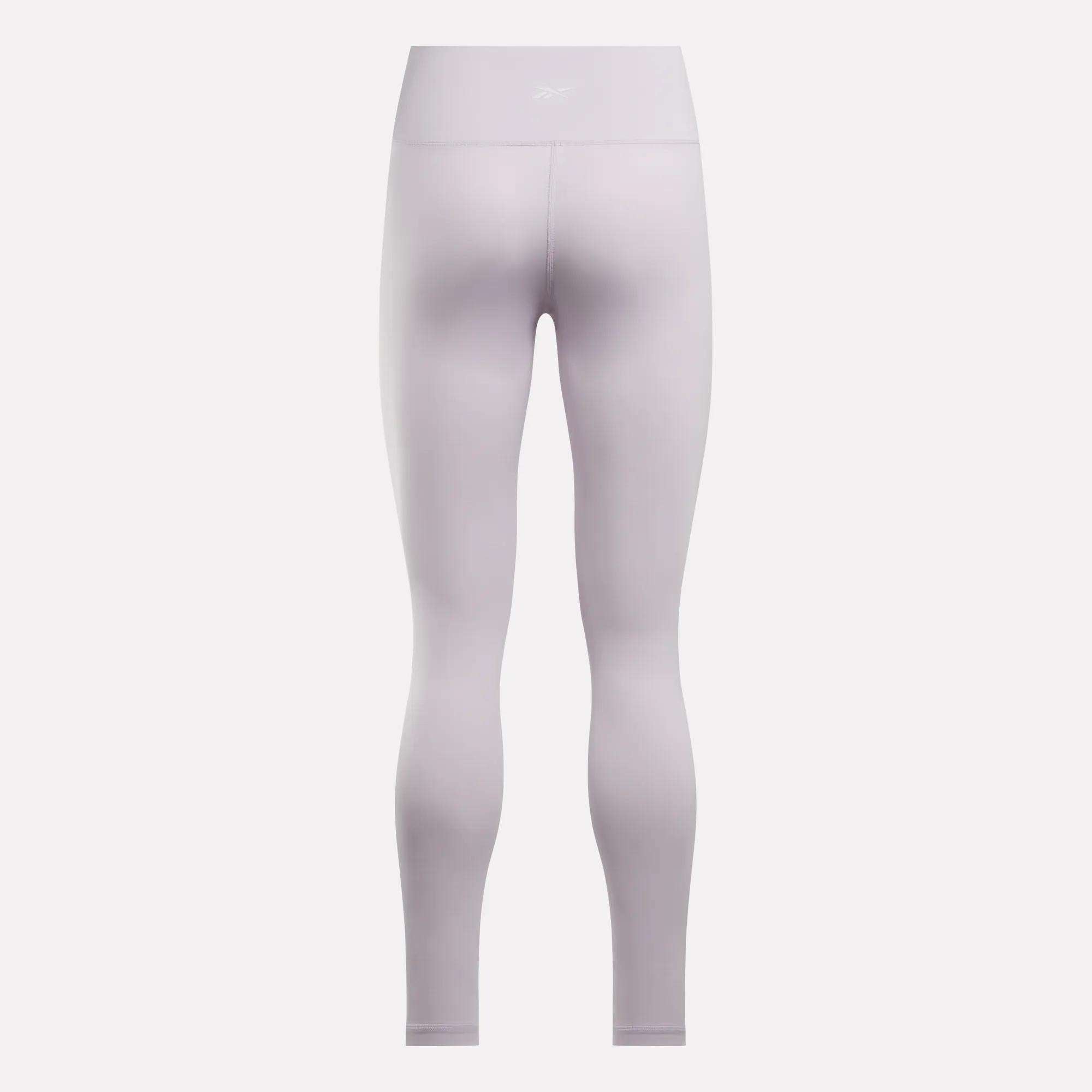 Back view of Reebok Women's Core High-Rise Leggings in light lavender, featuring RBK-DRY technology and a subtle logo on the waistband, displayed against a plain white background.