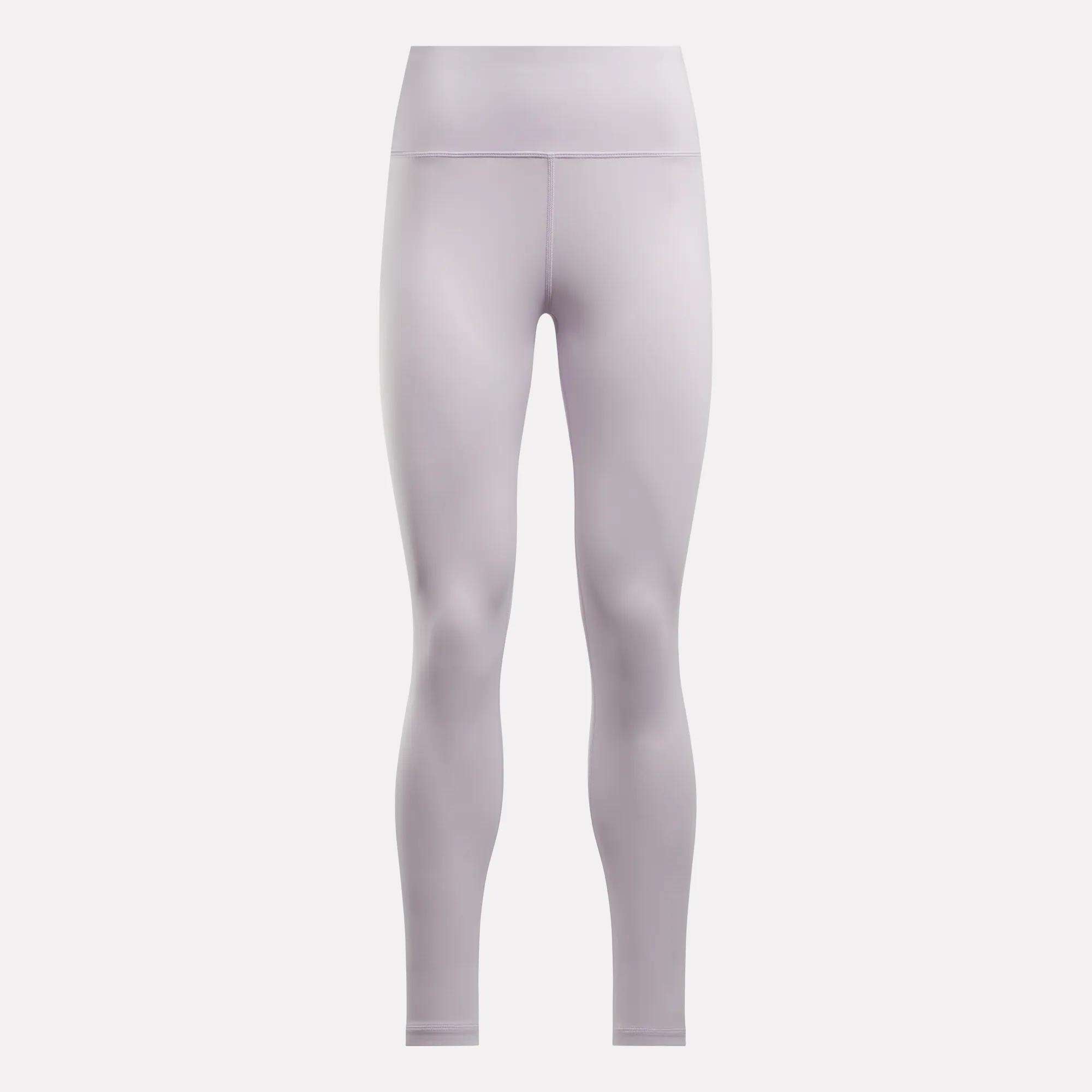 Reebok Women's Core High-Rise Leggings in light purple feature a seamless, smooth design with visible waist and leg stitching. Made with RBK-DRY fabric for comfort, shown on a plain, light background.