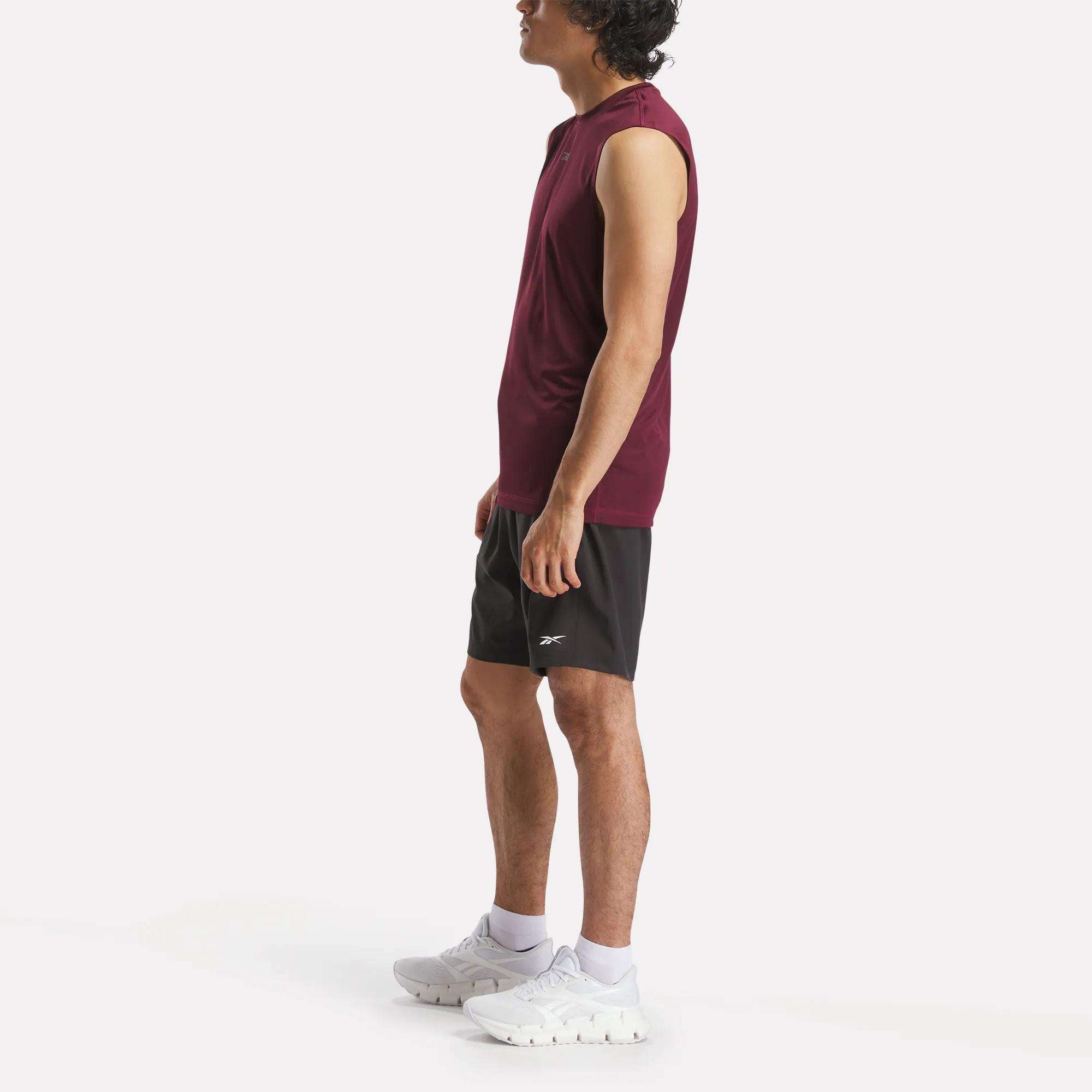 A man in profile wears a sleeveless burgundy athletic shirt, Reebok Men's Workout Ready Woven Shorts, white socks, and white athletic shoes against a plain white background.