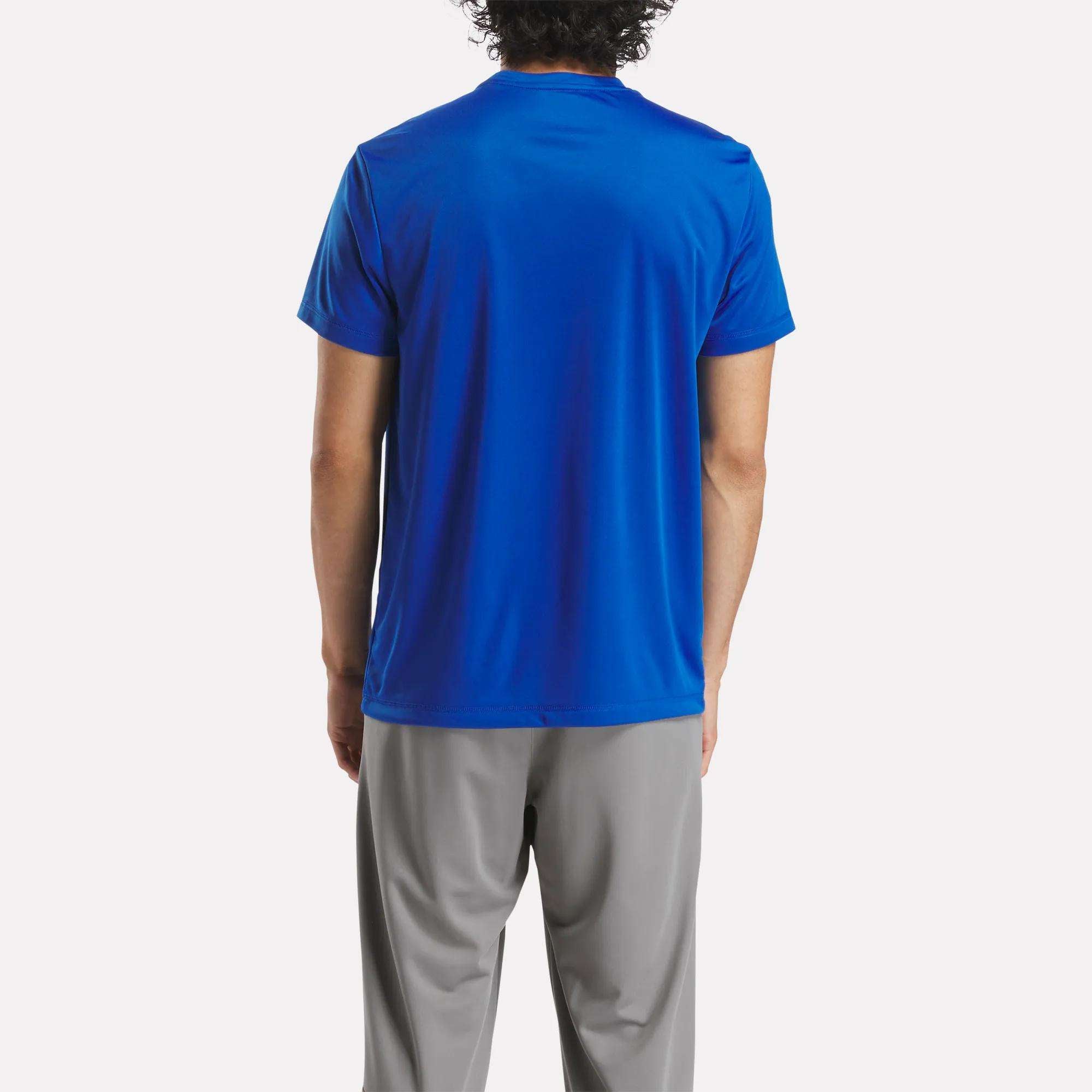 A person faces away, wearing a royal blue Reebok Men's ID Train Short Sleeve Tech Tee made from RBK-DRY fabric with light gray pants, standing against a plain white background.