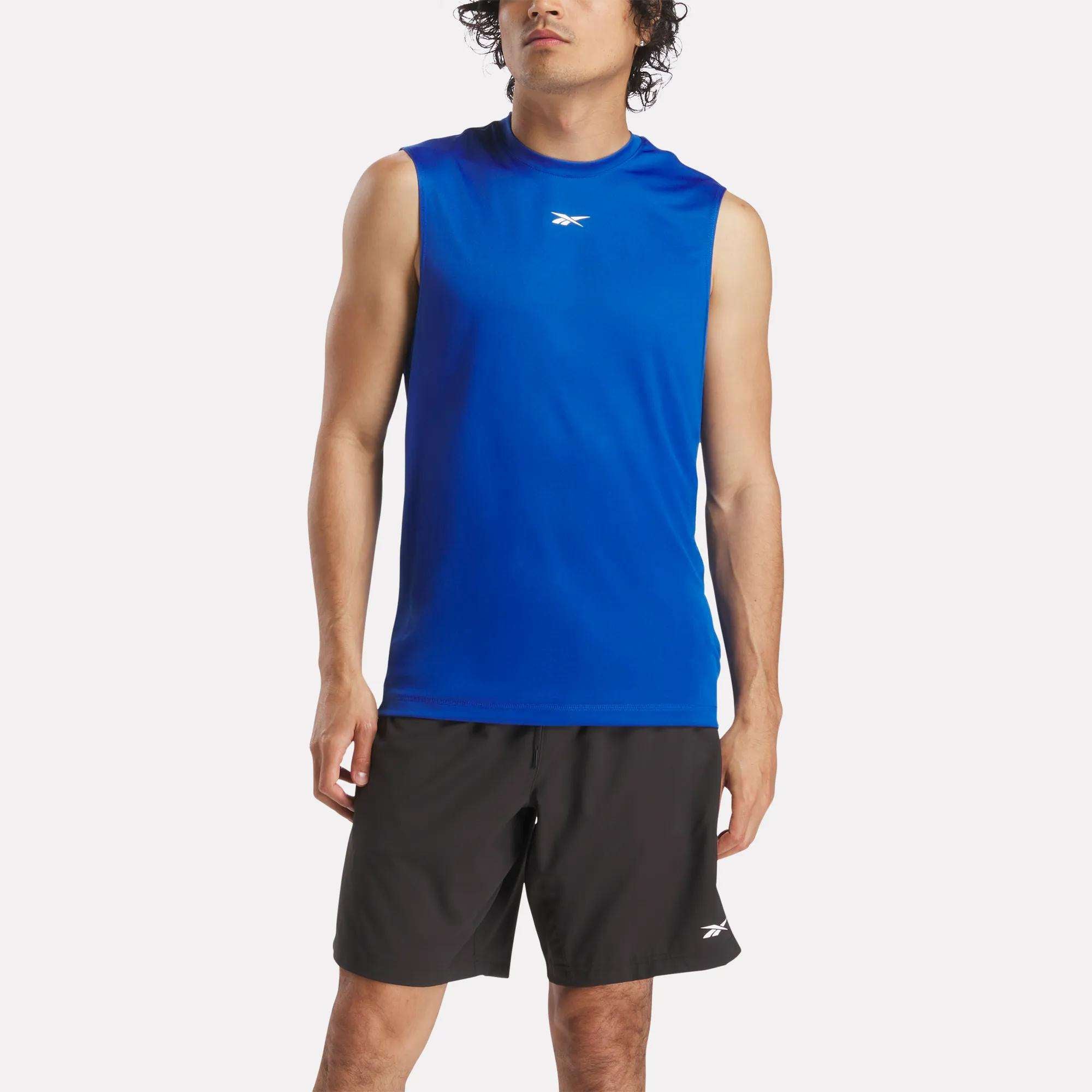 A man stands against a white background wearing the Reebok Men's Train Sleeveless Tech Tee in blue lightweight polyester and black shorts, both displaying the Reebok logo.