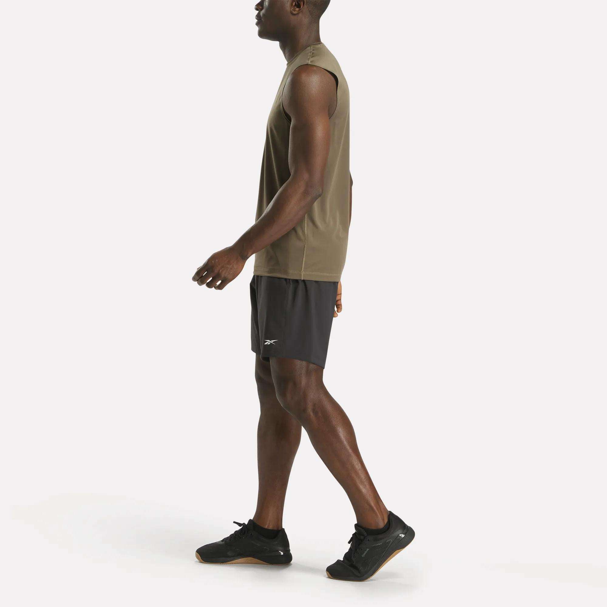 A man in a Reebok Men's Train Sleeveless Tech Tee, lightweight polyester jersey, with black athletic shorts and black sneakers walks in side profile against a white background.