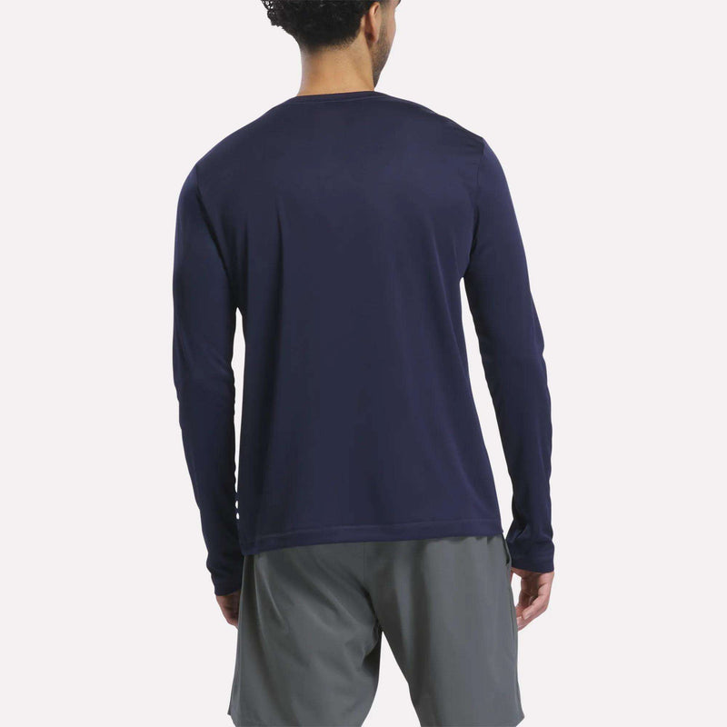 A man stands facing away, wearing a Reebok Men’s Long Sleeve Tech T-Shirt in navy and gray shorts against a plain white background—ideal for cold weather workouts.