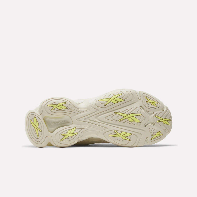 The image shows the bottom view of Reebok Women's DMX Series 3000 Training Shoes, featuring a beige sole with wavy tread patterns, yellow accents, and textured grip. The design highlights comfort with cushioned support and DMX 3 Technology.