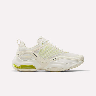 The Reebok Women's DMX Series 3000 Training Shoes are white athletic sneakers with light yellow accents, mesh panels, and a chunky sole featuring a visible green heel air cushion and DMX 3 Technology for advanced comfort.