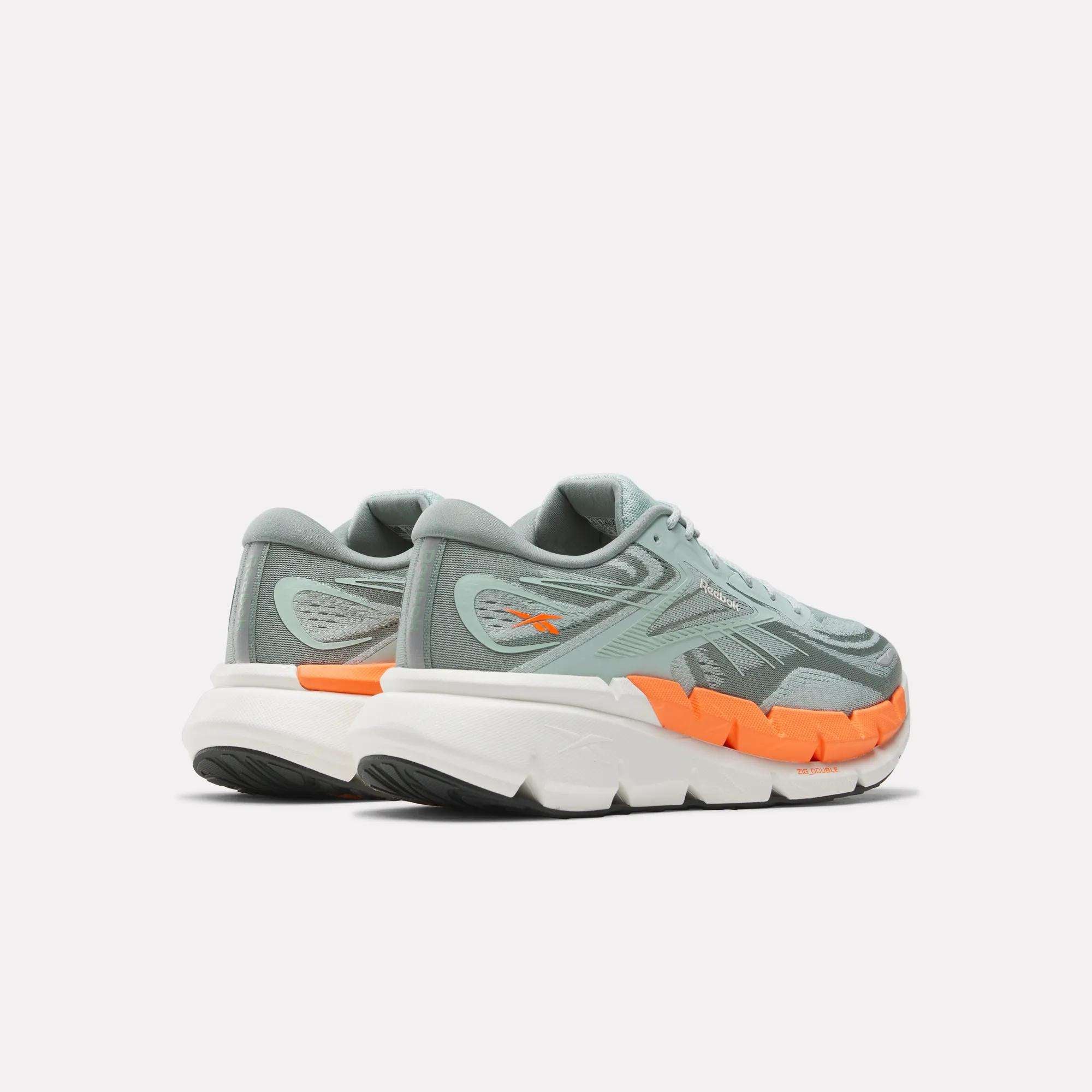 A pair of men's Reebok FloatZig Double running shoes in light grey with cushioned thick white soles, orange midsole accents, and black tread are shown side by side, toes right and heels left, against a plain white background.