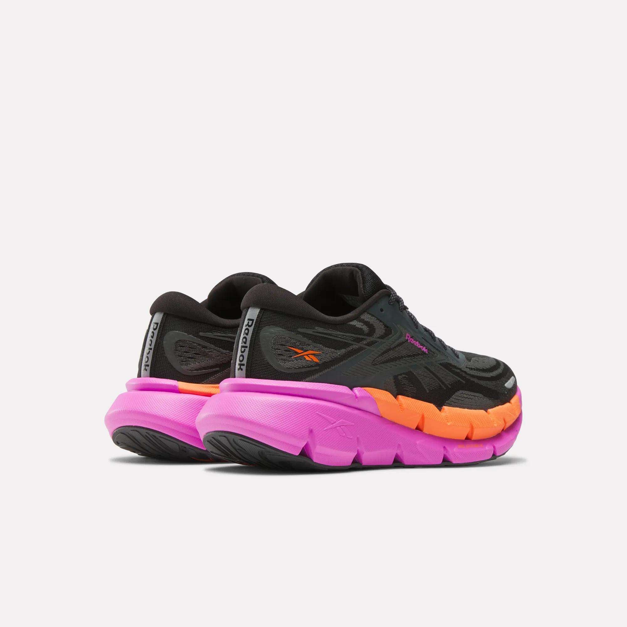 A pair of Women's FloatZig Double Running Shoes by Reebok, featuring black uppers and thick, chunky soles in bright pink and orange, shown from the back and side on a plain white background.