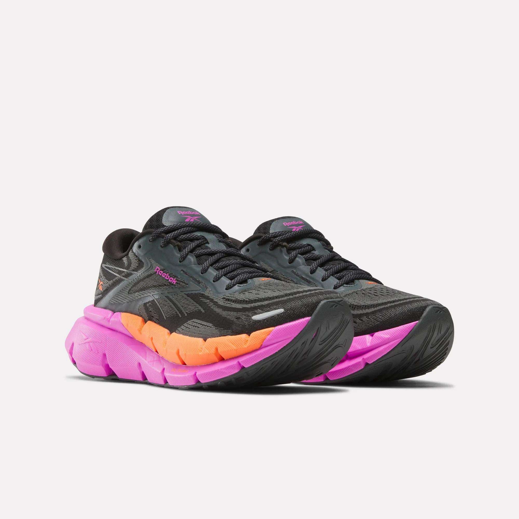 The Reebok Women's FloatZig Double Running Shoes feature a black upper with subtle pink and purple accents, plus pink-to-orange gradient soles. Displayed on a white background, they deliver max cushioning for comfortable runs.