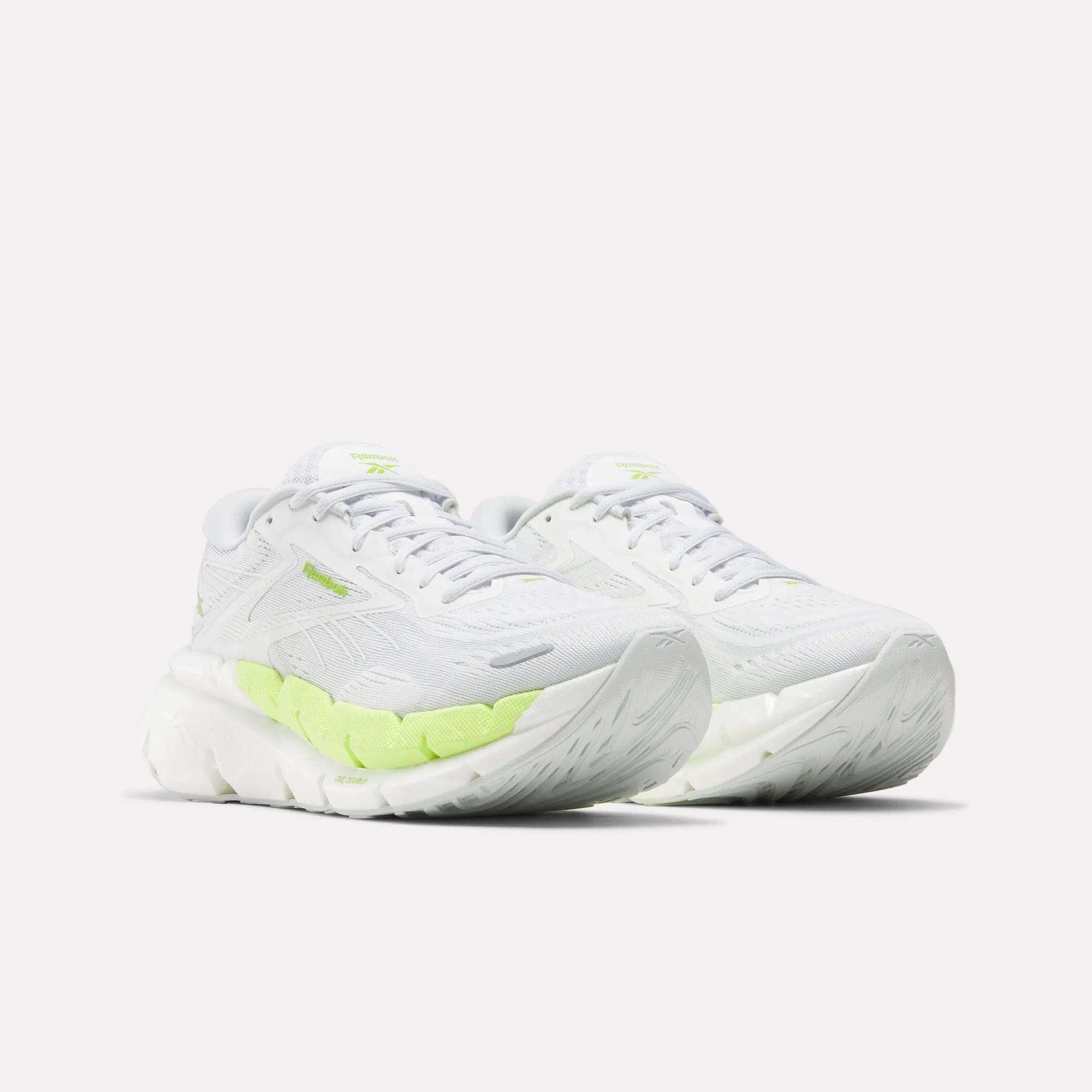 A pair of Women's FloatZig Double Running Shoes by Reebok in white, featuring chunky soles, neon green accents, and mesh panels for maximum cushioning—perfect for long runs. Displayed against a plain white background.