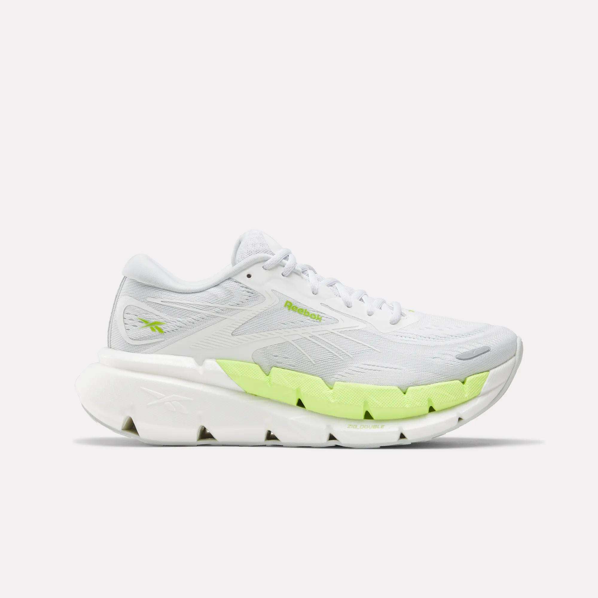 The Reebok Women's FloatZig Double Running Shoe features a thick, segmented sole and neon yellow accents for max cushioning, shown in white from the side against a plain background.