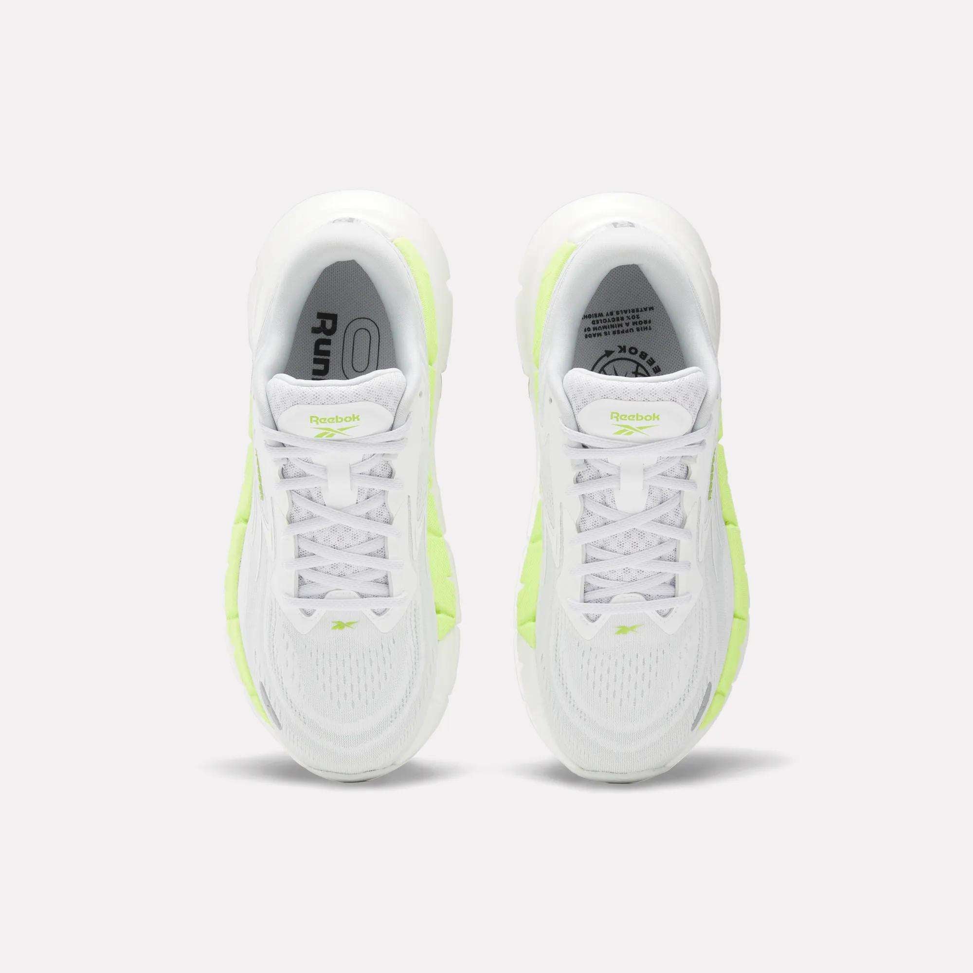 Top view of a pair of Women's FloatZig Double Running Shoes by Reebok in white with neon yellow accents, displayed side by side on a light background—ideal max-cushioned sneakers for runners seeking comfort.