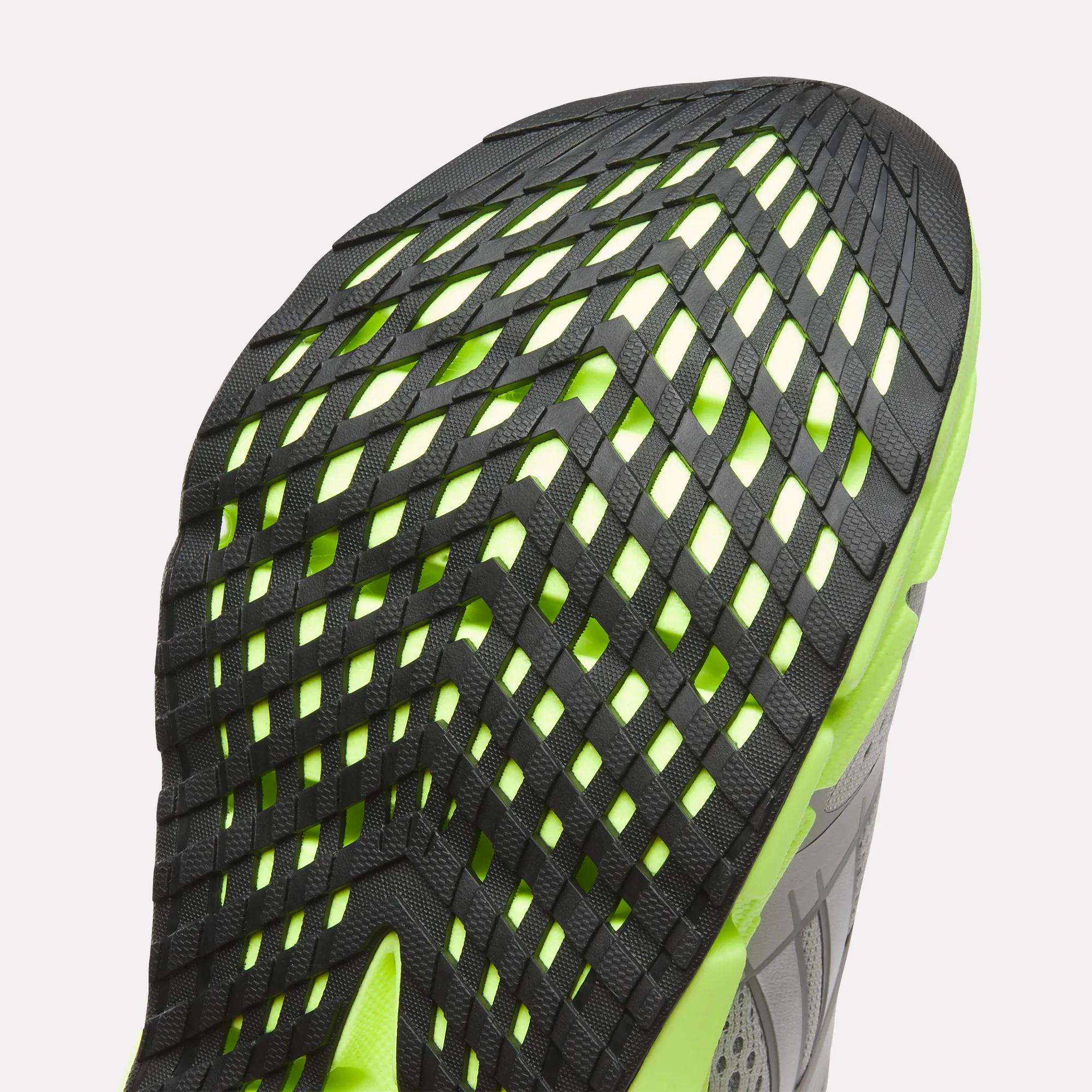 Close-up of the sole on Reebok Women's FloatZig 2 Running Shoes, showcasing a unique black grid tread over neon green with Superfloat+ cushioning; part of the gray upper is also visible.