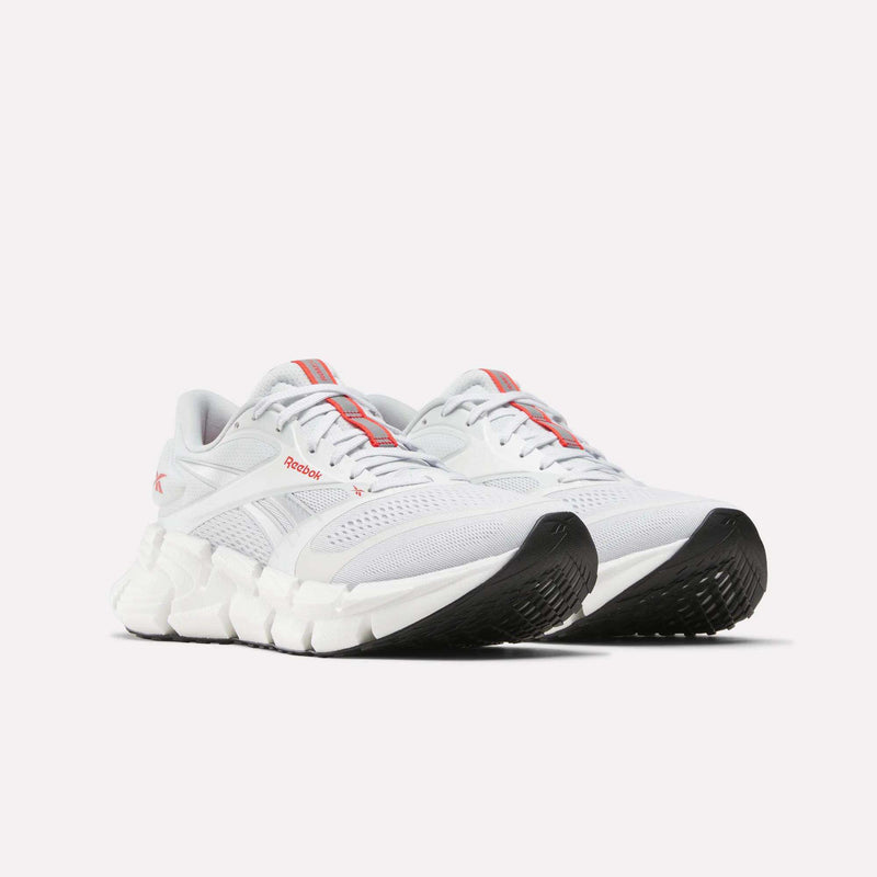 A pair of Reebok Men's FloatZig 2 Running Shoes in white, highlighted with red accents, mesh uppers, and distinctive chunky black and white soles—engineered for running with energy-returning cushioning—are displayed side by side on a plain light background.