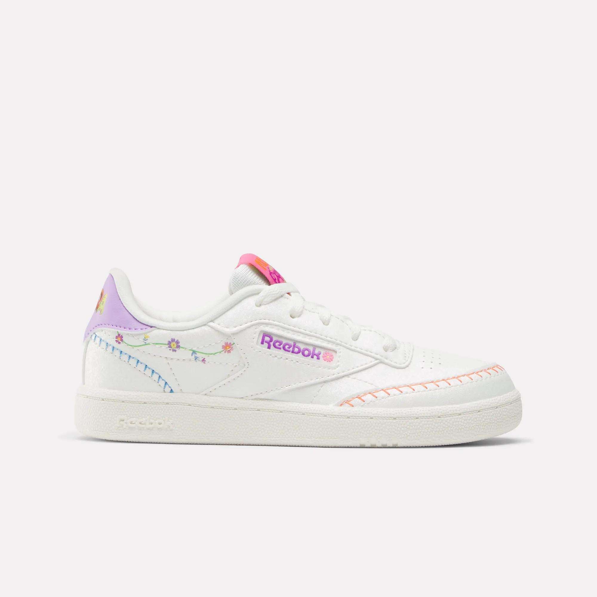 The Reebok x DORA Club C Shoes for little kids feature pastel rainbow accents, floral embroidery, a pink logo, and orange stitching on white—perfect colorful shoes by Reebok for playful style.