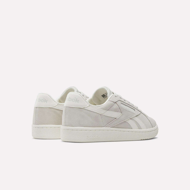 Two off-white Reebok Women's Club C Grounds UK Shoes with side stripes and textured soles are displayed on a light background. One shoe faces forward, while the other is angled to reveal the back and side.