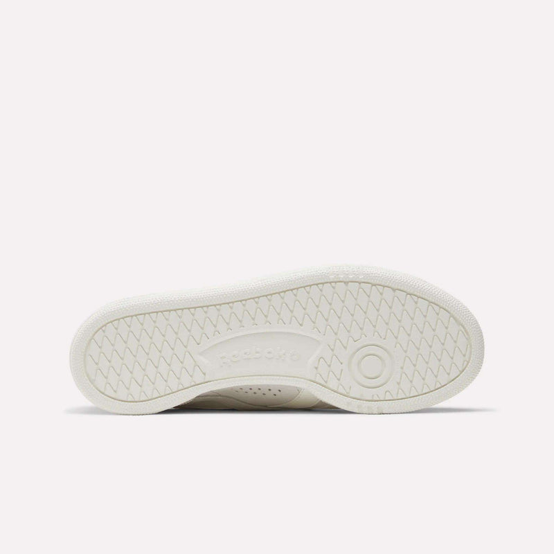 The image shows the white sole of the Reebok Women's Club C Grounds UK Shoes lying flat, with a herringbone tread pattern and an embossed Reebok logo at the center.