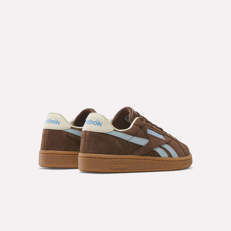 The Reebok Women's Club C Grounds UK Shoes are brown retro sneakers with light blue and white accents, suede material, blue stripes, and Reebok logos on the heel and side, displayed against a plain white background.