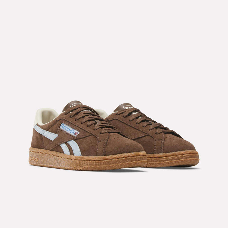 A pair of Reebok Women's Club C Grounds UK brown suede shoes with white side stripes, gum rubber soles, and Reebok logos on the side and tongue, displayed against a plain white background.