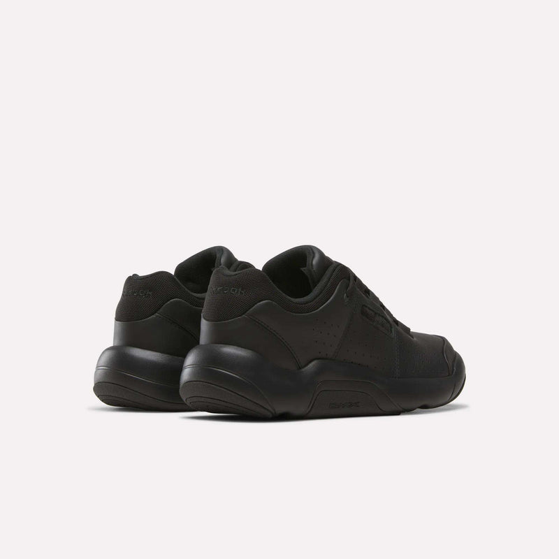 A pair of Reebok Dmx Comfort + Classic sneakers in black with low-top design, crafted from premium leather, shown from a rear angled view against a plain white background.