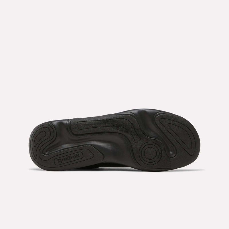 Black rubber outsole of the Reebok Dmx Comfort + Classic walking shoe, featuring textured, wavy patterns and an embossed Reebok logo near the heel, displayed against a plain white background—crafted to complement premium leather uppers and enhanced with dynamic air cushioning for superior comfort.
