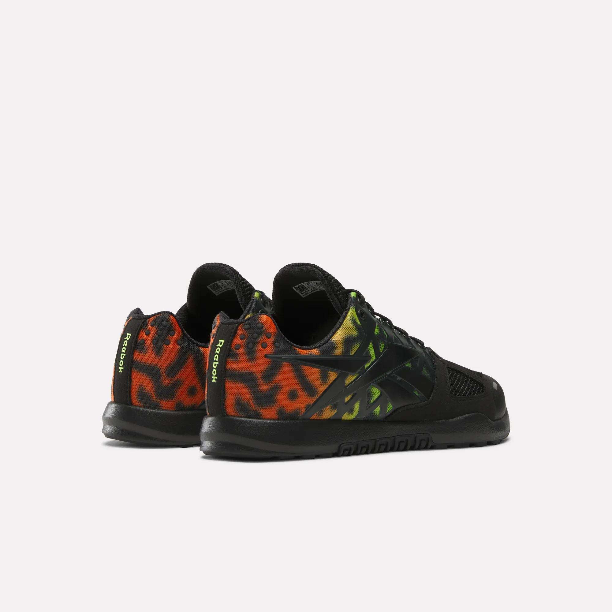 The Reebok Men's Nano 2.0 Training Shoes feature a black base with a striking red, orange, and yellow gradient flame pattern on the sides and heel, plus “REEBOK” in yellow on the heel tab—ideal for functional fitness.