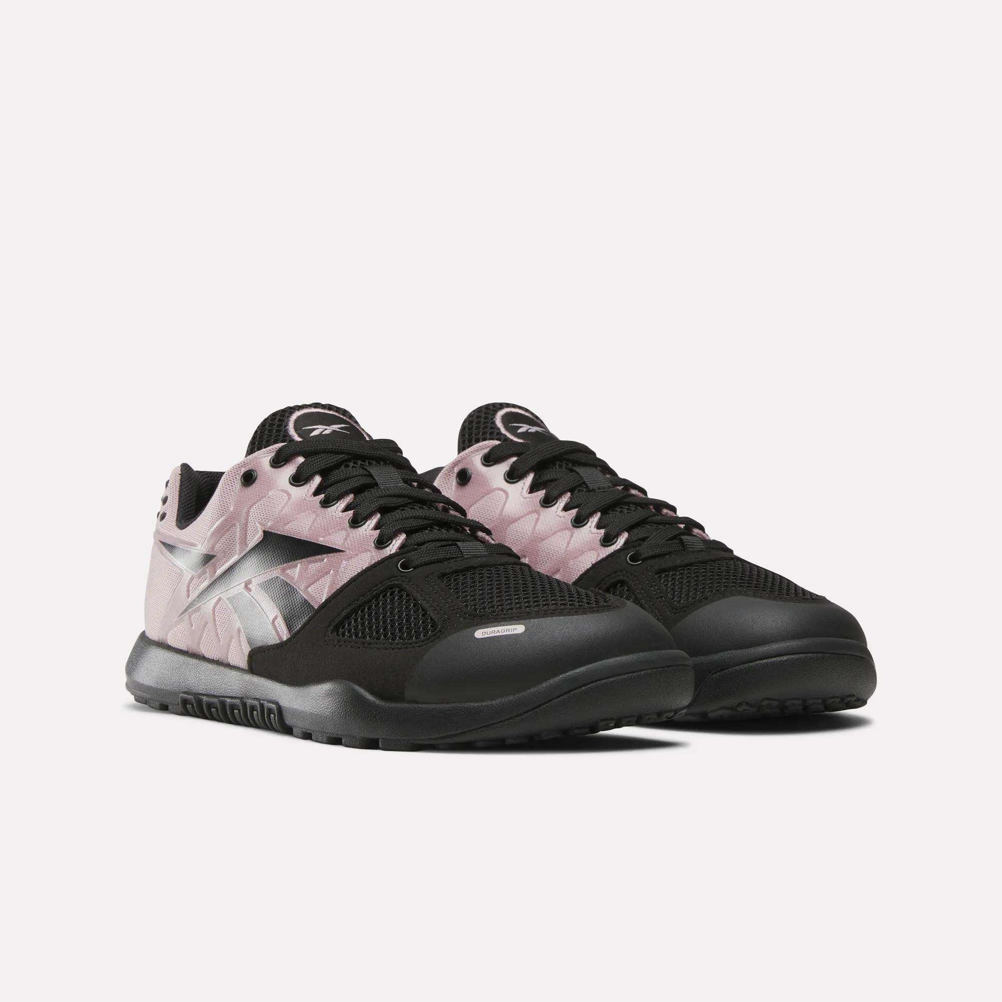 The Reebok Women's Nano 2.0 Training Shoes feature black soles, mesh uppers, light pink side panels, and a silver Reebok logo—ideal for functional fitness. Displayed on a light background, they are angled slightly to the right.