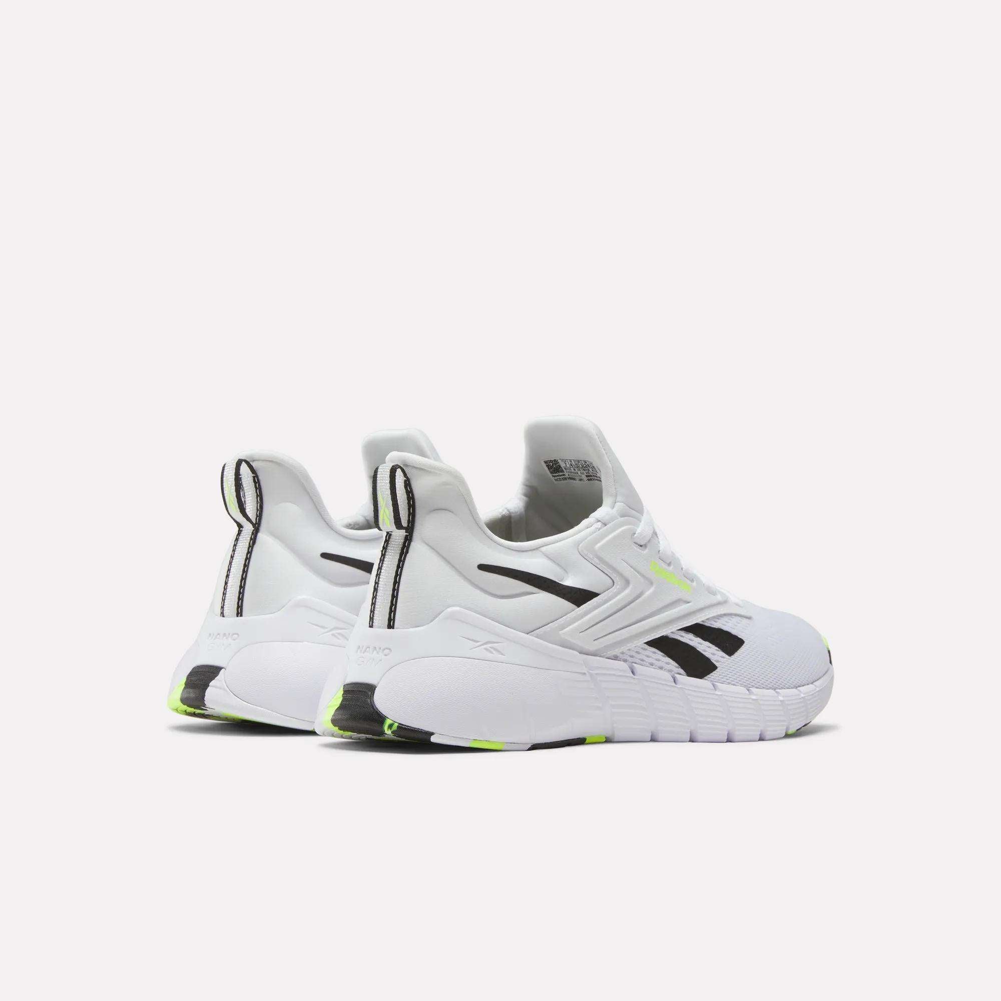 Reebok Women's Nano Gym Training Shoes in white with black accents, thick soles, and neon yellow details, designed for weight training. Shown from an angled rear view on a plain light background.
