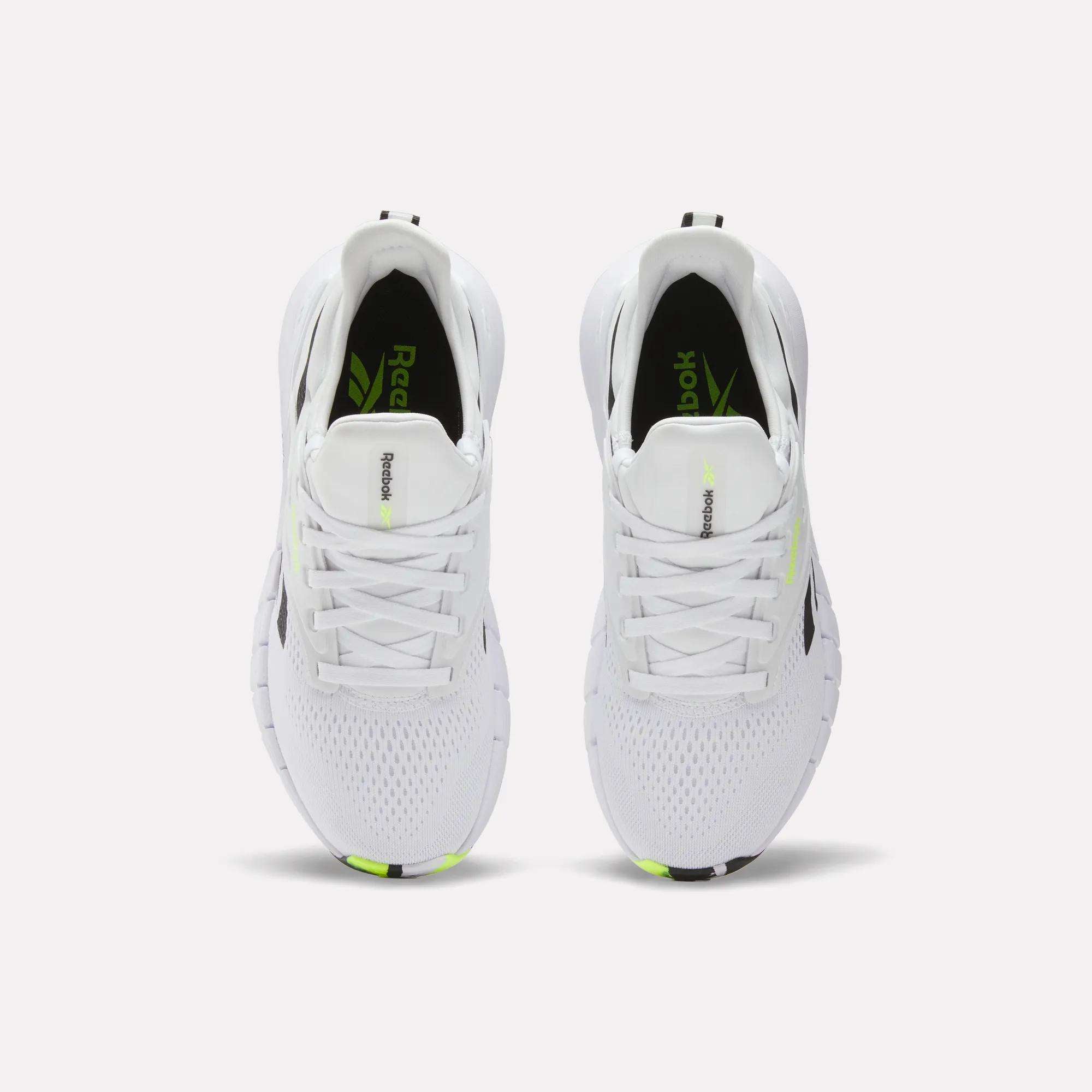 A pair of white Reebok Women's Nano Gym Training Shoes viewed from above, featuring mesh uppers, white laces, black and neon yellow accents, plus the Reebok logo on the insoles and tongues.
