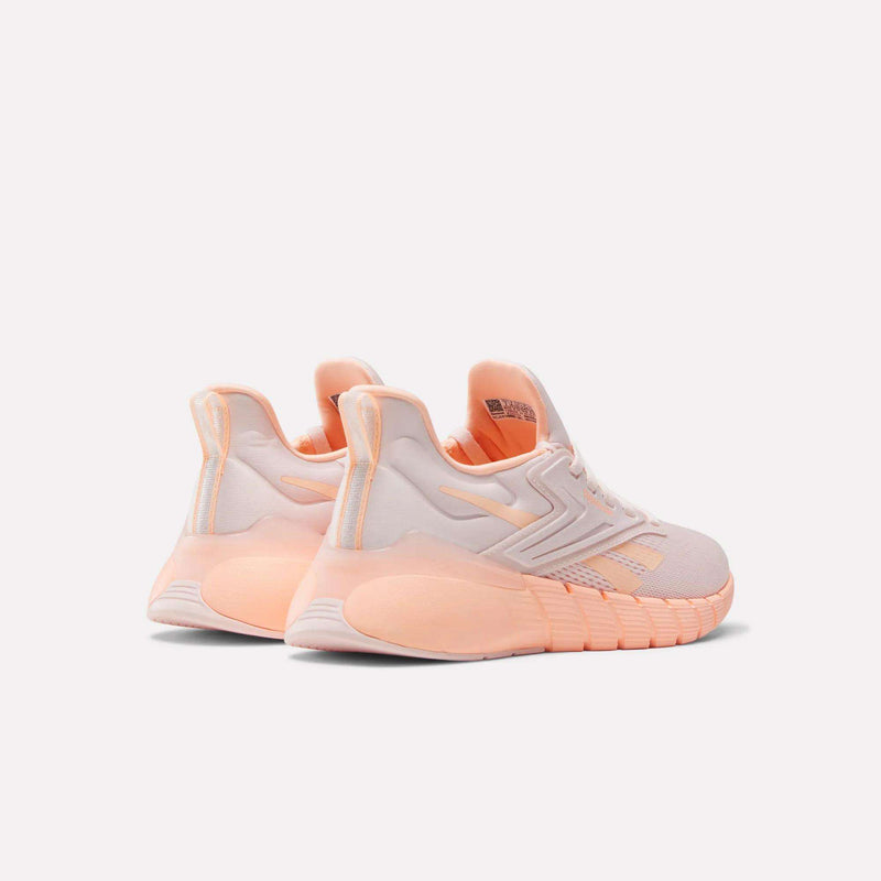 A pair of Reebok Women's Nano Gym Training Shoes in pastel pink and peach, featuring a chunky, textured sole, displayed from the back at an angle on a plain light background.
