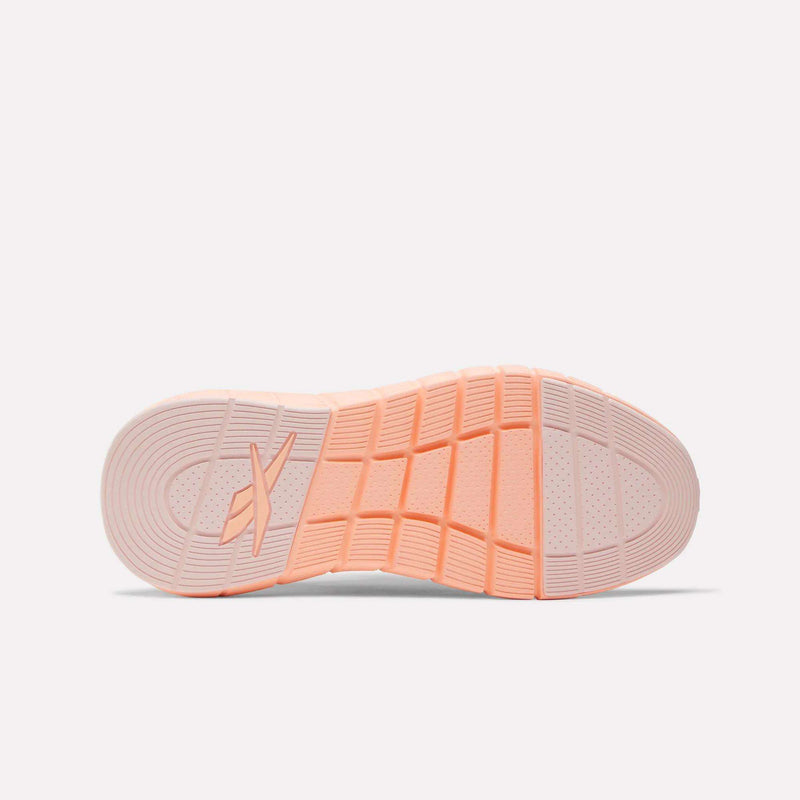 The image displays the sole of Reebok Women's Nano Gym Training Shoes in light pink, featuring grooved traction patterns and a stylized X logo by the arch on a plain white background.