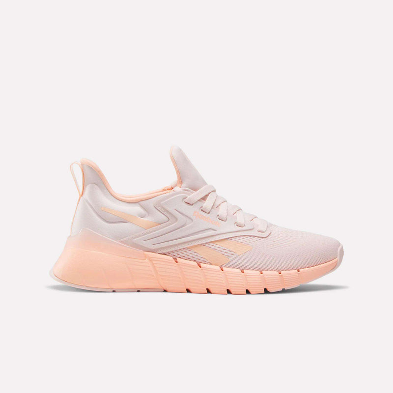 The Reebok Women's Nano Gym Training Shoes feature a light pink mesh upper, peach accents, textured sole, and heel pull tab—perfect cross-training shoes shown against a plain white background.
