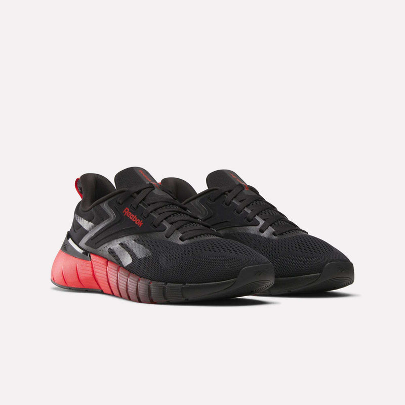 A pair of Reebok Men's Nano Gym Training Shoes in black with red accents and soles, featuring a mesh upper and reflective details, displayed on a plain white background.