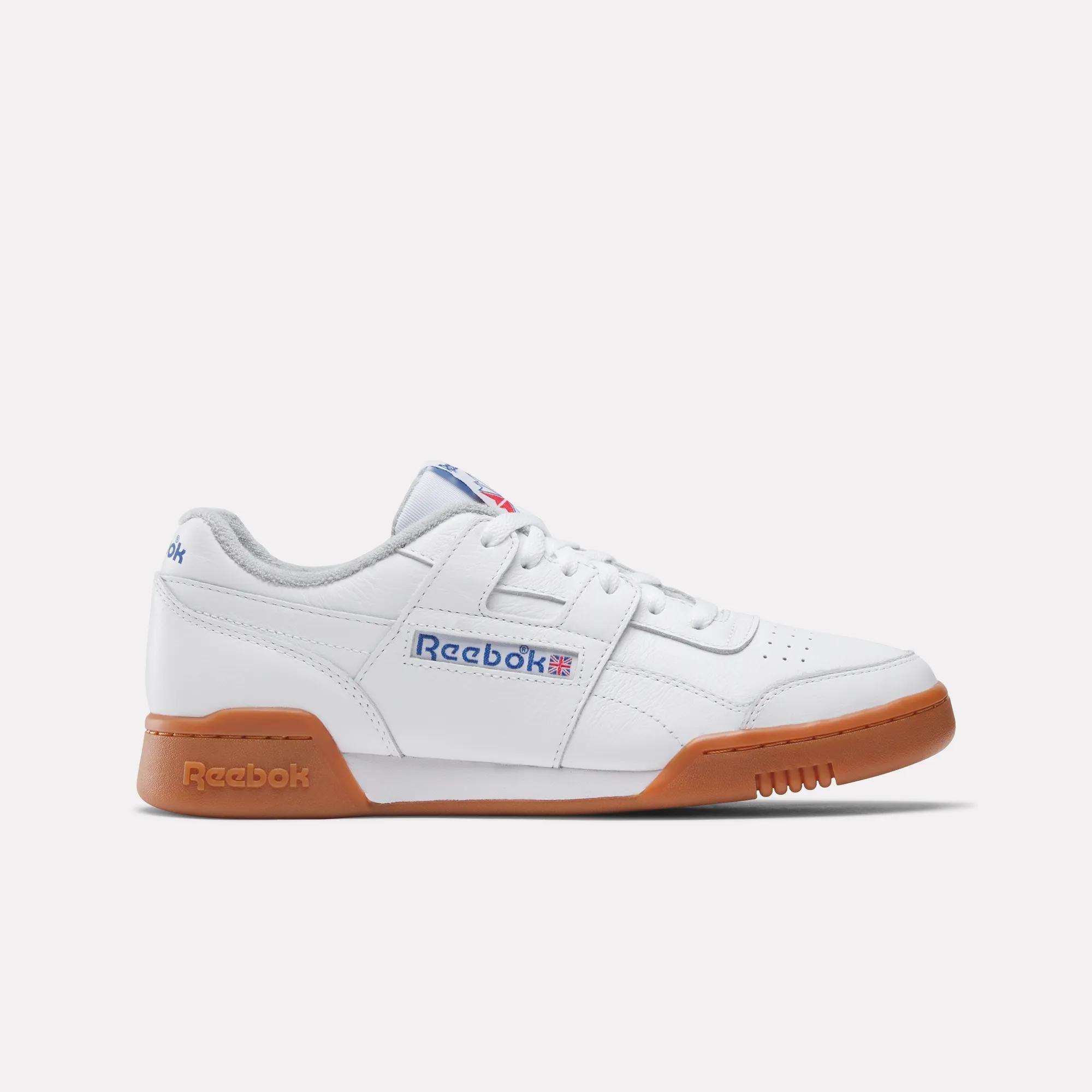 The Reebok Women's Workout Plus Shoes feature a white upper, gum sole, blue and red side logo, and white laces—shown in profile on a plain light background for classic '80s-inspired style.