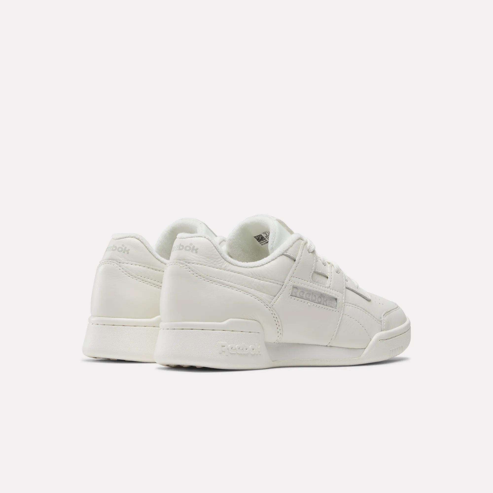 A pair of Reebok Women's Workout Plus Shoes in white, featuring low tops, laces, and subtle gray side branding—ideal for women's fitness—shown from the back and side on a plain white background.