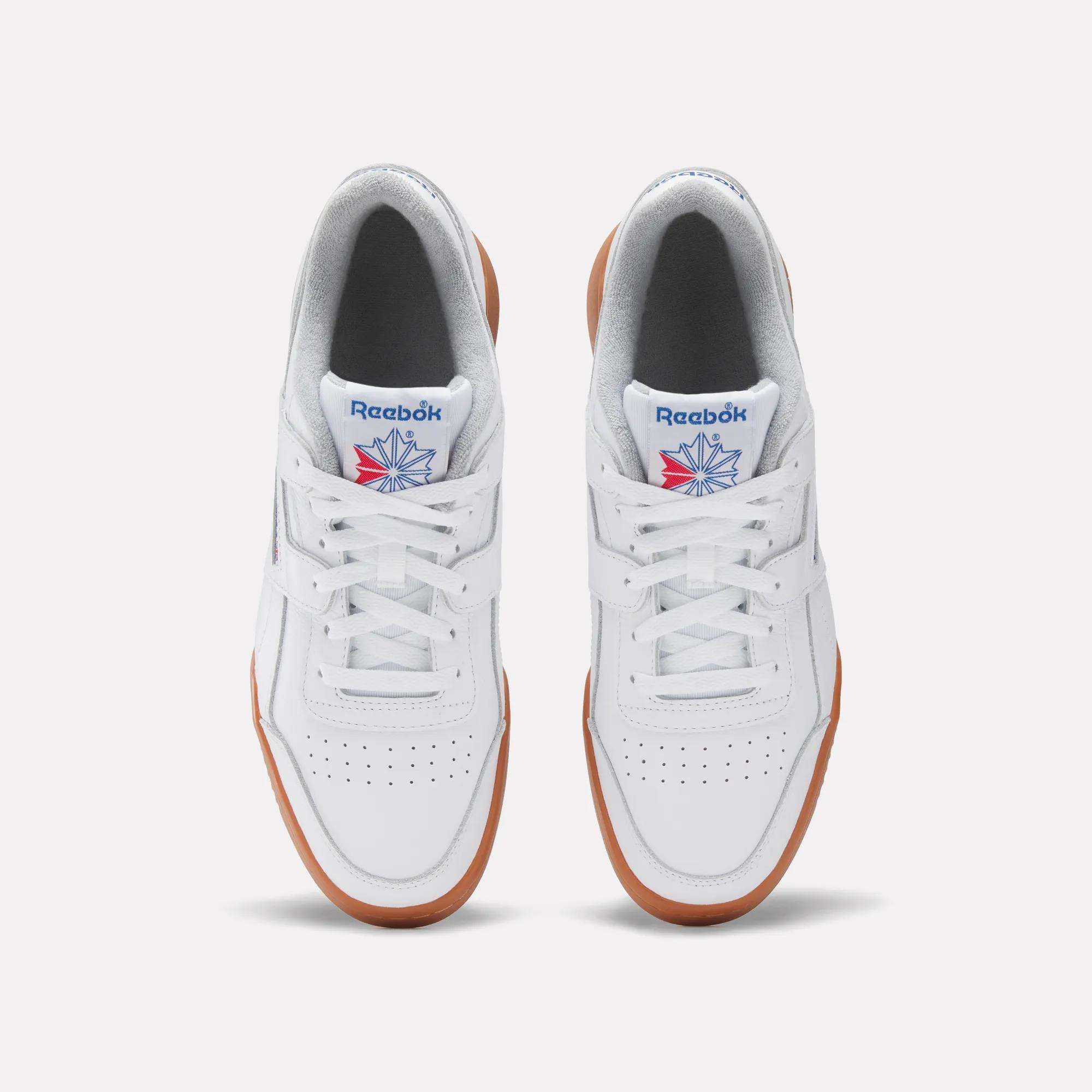 A pair of Reebok Workout Plus Shoes in white with gum soles, seen from above. Featuring white laces, perforated toe boxes, and the classic Reebok logo with blue and red accents on the tongues—an iconic '80s fitness look.