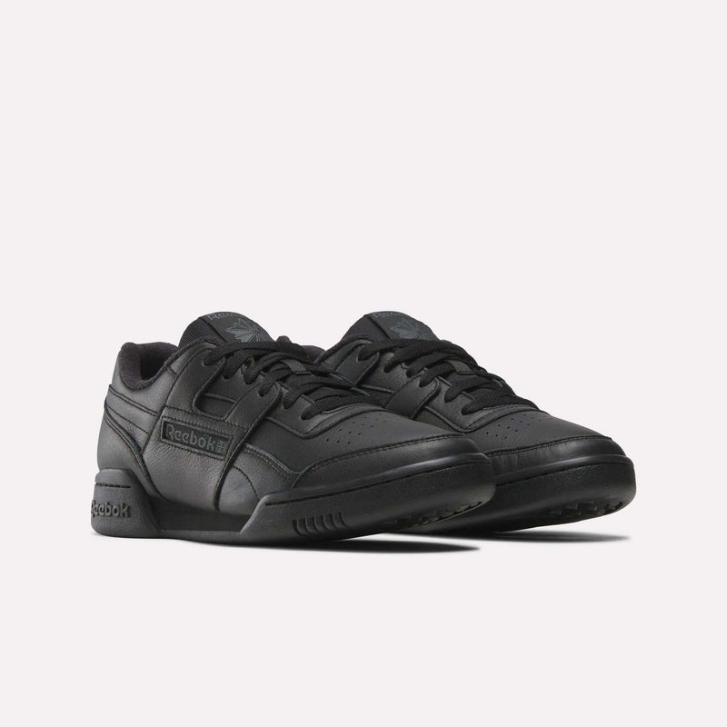 A pair of Reebok Workout Plus Shoes in black, showcasing a low-top design with the Reebok logo on the side and a textured sole for grip—ideal for classic ’80s fitness style. Displayed against a plain white background.