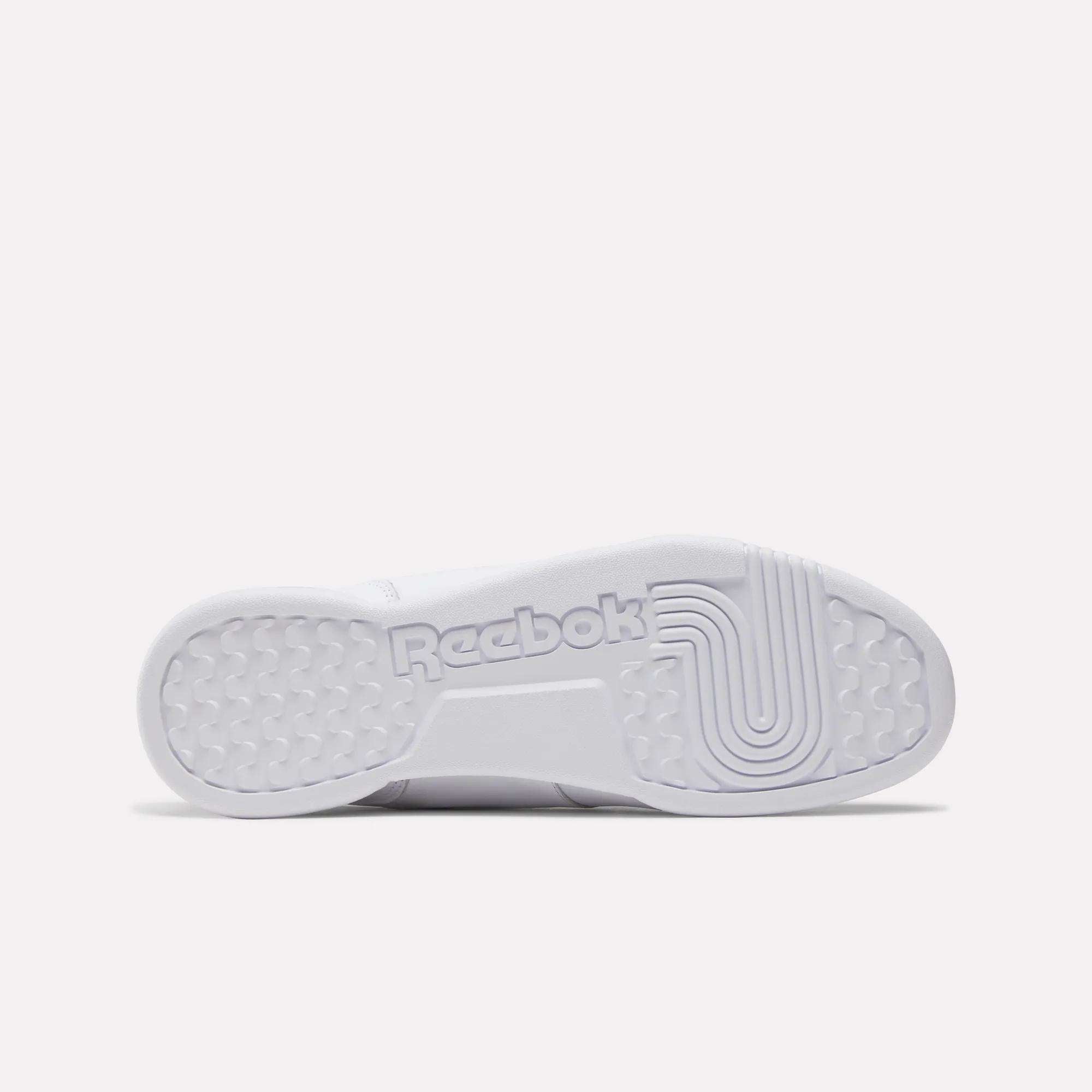 The image displays the white sole of the Reebok Workout Plus Shoes, showing the Reebok logo, textured grip patterns, circular treads at the heel, and linear grooves at the forefoot—details inspired by classic 1980s fitness style.
