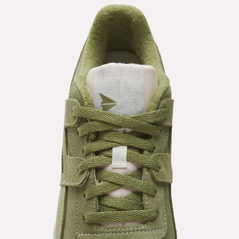 Top view of olive green Reebok Workout Plus Shoes with suede texture, matching laces, and an embossed Reebok logo with a star on the tongue. The light beige tongue and lining highlight this classic '80s fitness style.