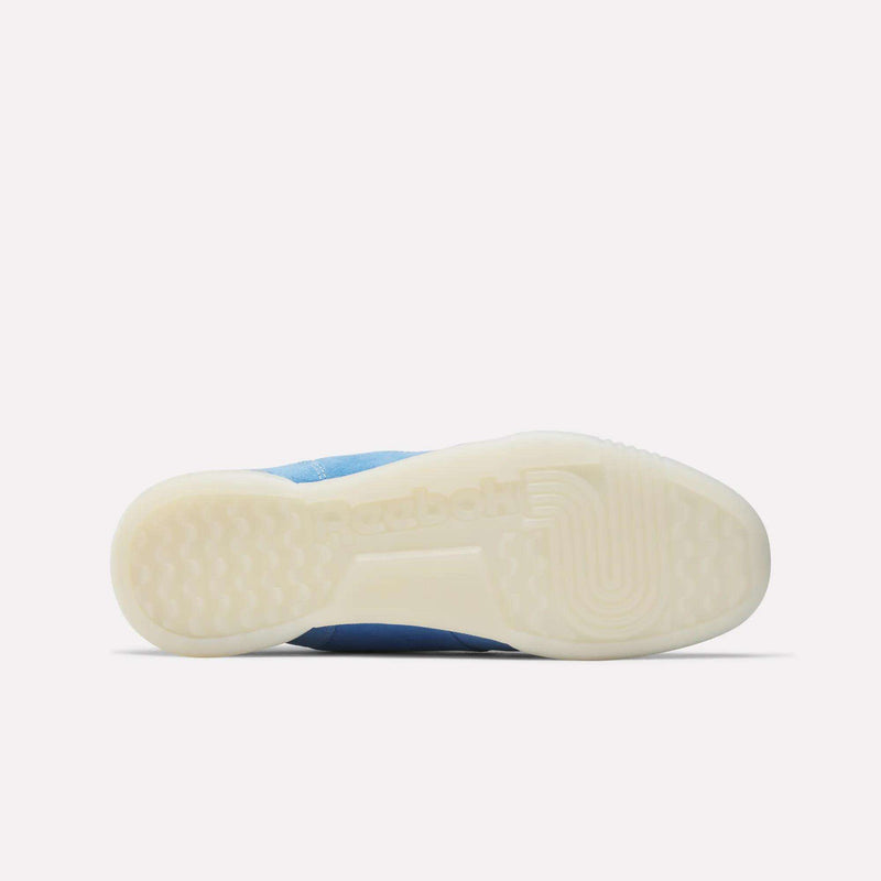 The image displays the bottom view of Reebok Workout Plus Shoes, highlighting a translucent white sole with textured grip and the Reebok logo embossed at the center, reflecting classic '80s fitness style in this light blue design.