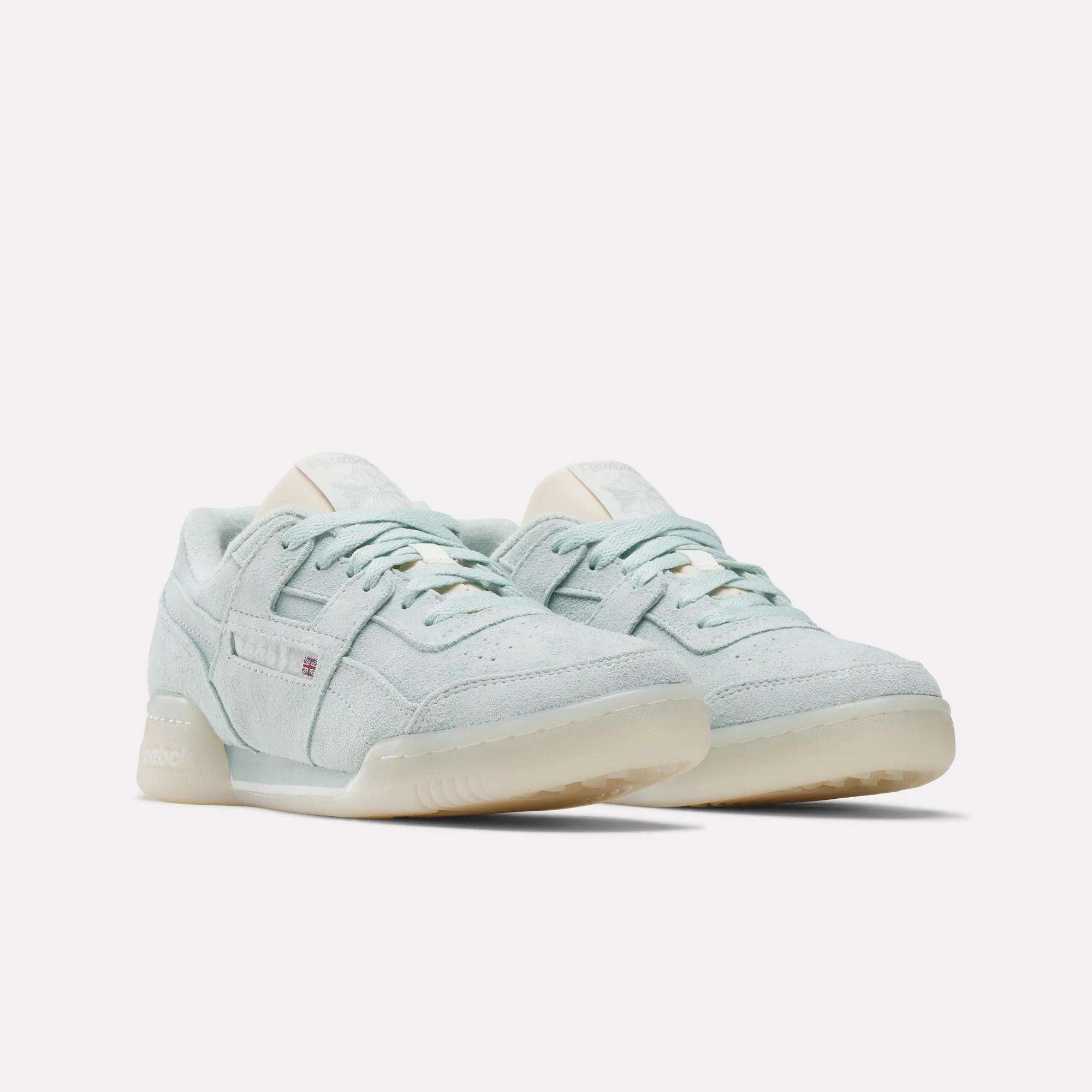 The Reebok Women's Workout Plus Shoes feature a classic low-top design with light blue suede uppers, off-white soles, and subtle '80s-inspired branding, displayed against a plain white background.